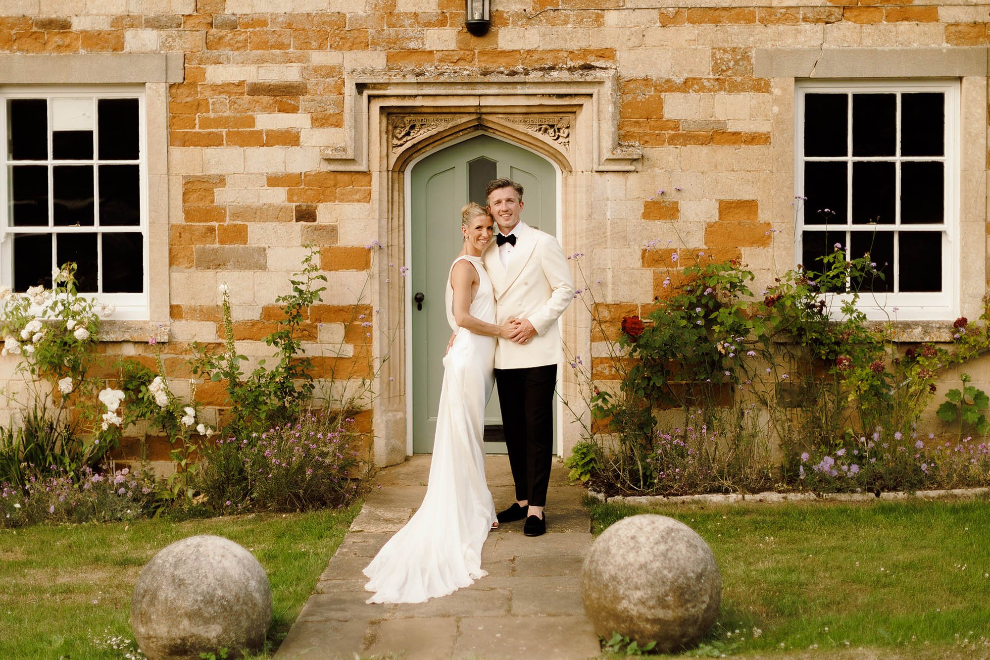 bride in danielle frankel and groom in white suit supply tuxedo pose for photo