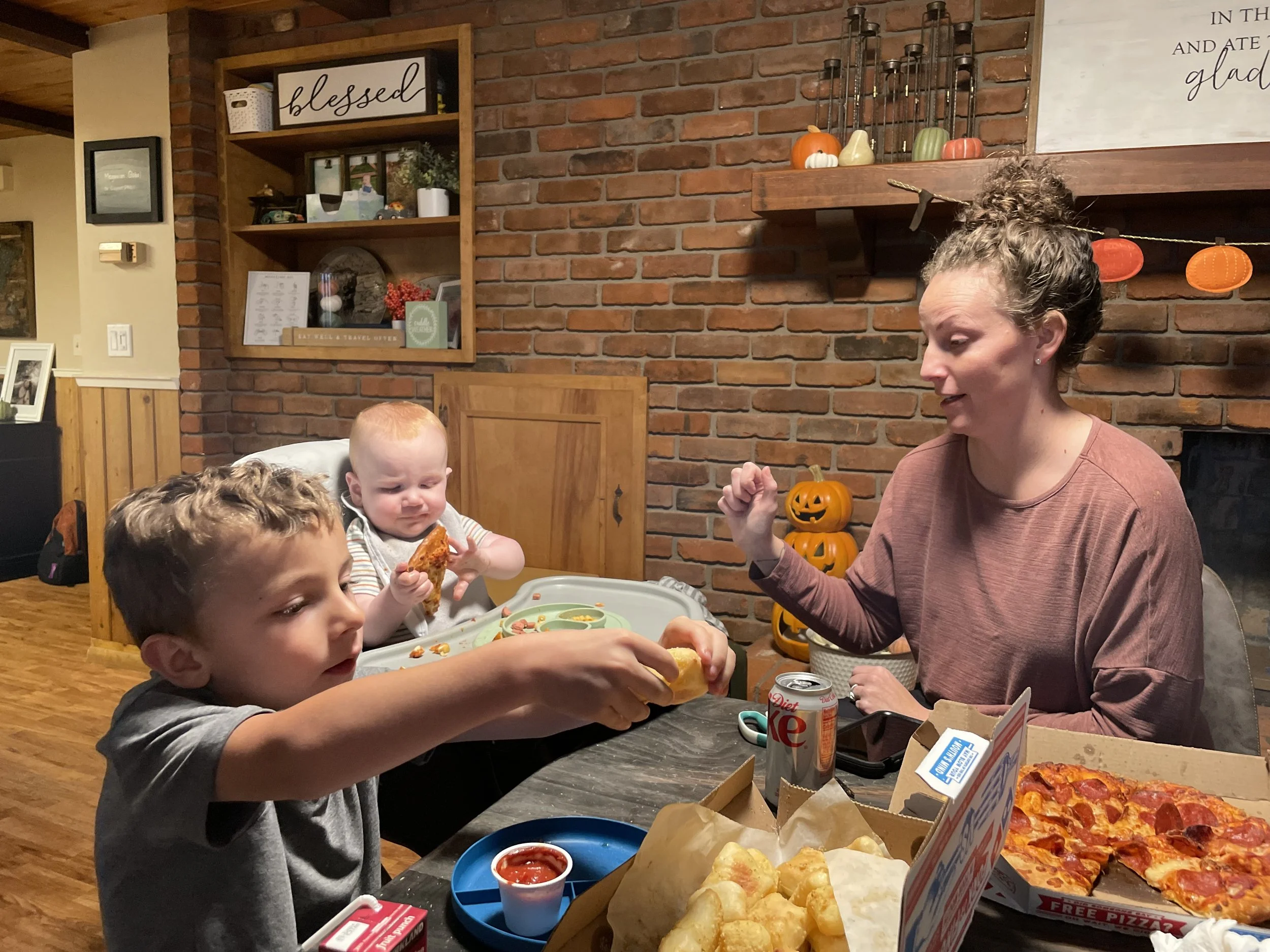 woman, child, and baby eating pizza at a table
