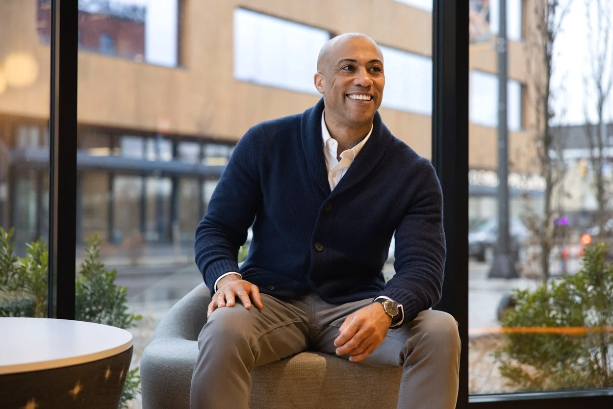 Executive portrait of a business leader seated by a window, captured during a natural unguarded moment with a genuine expression.