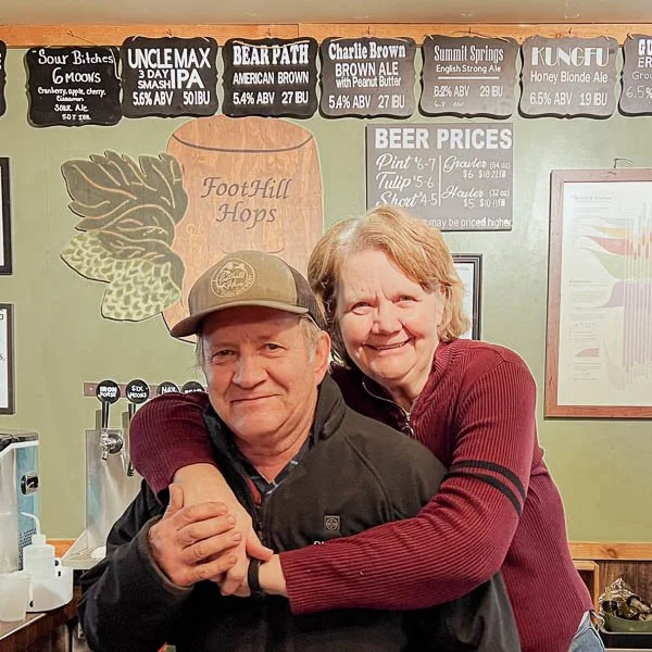 Husband and wife small business owners standing together inside their brewery, representing local entrepreneurship and community support.