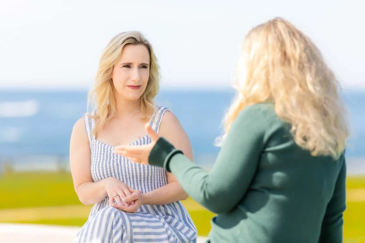 Laurie Nicoletti, a wellness coach based in Newport, RI, talking with a client outdoors near the ocean, showcasing her approachable coaching style