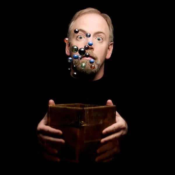 Portrait from the REVEALED project featuring a man holding a wooden box as marbles appear suspended in motion, representing personal meaning, curiosity, and self-discovery.