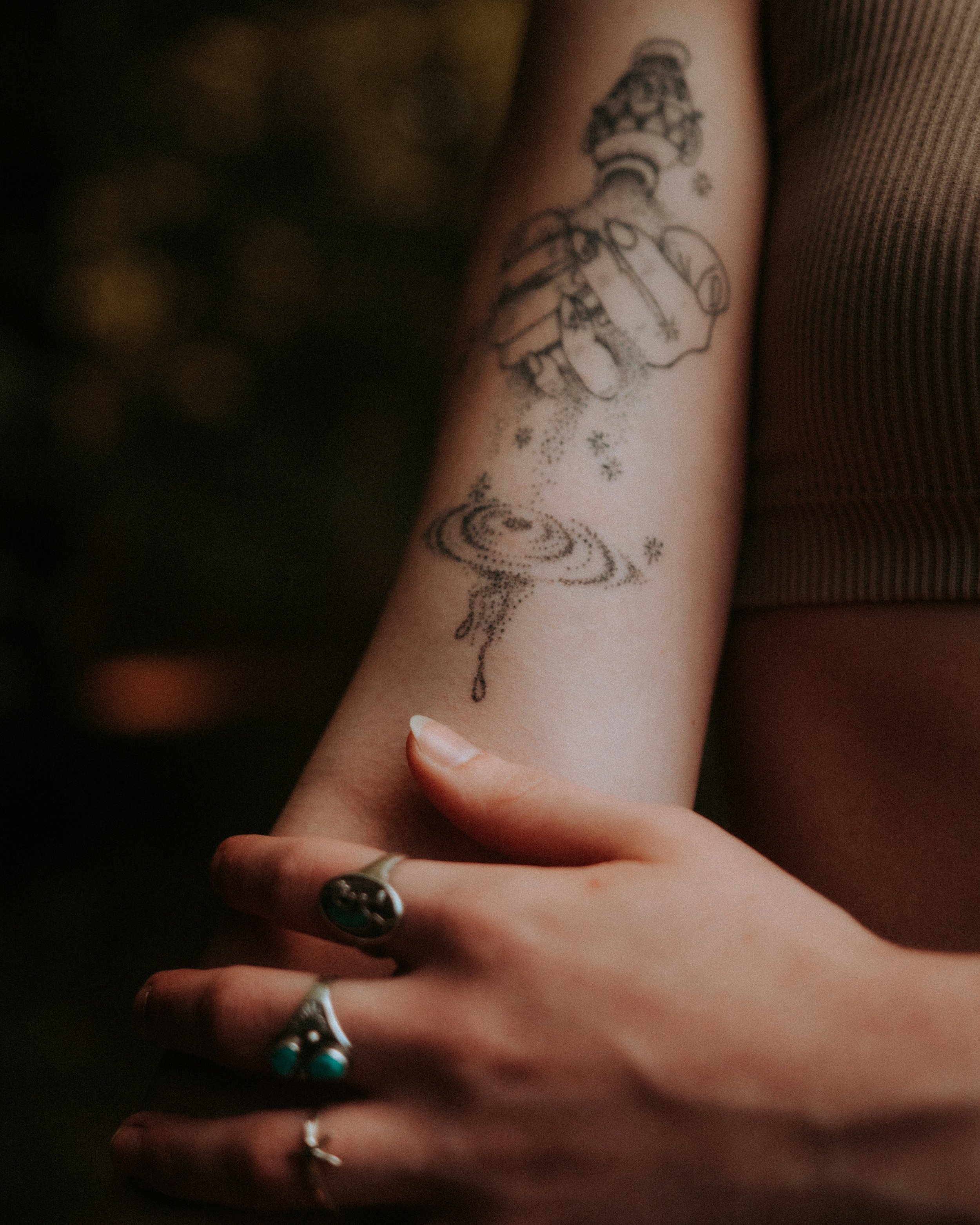 Close-up of a person's arm with a tattoo of a chess piece, surrounded by small snowflake symbols, and decorated with rings on fingers.