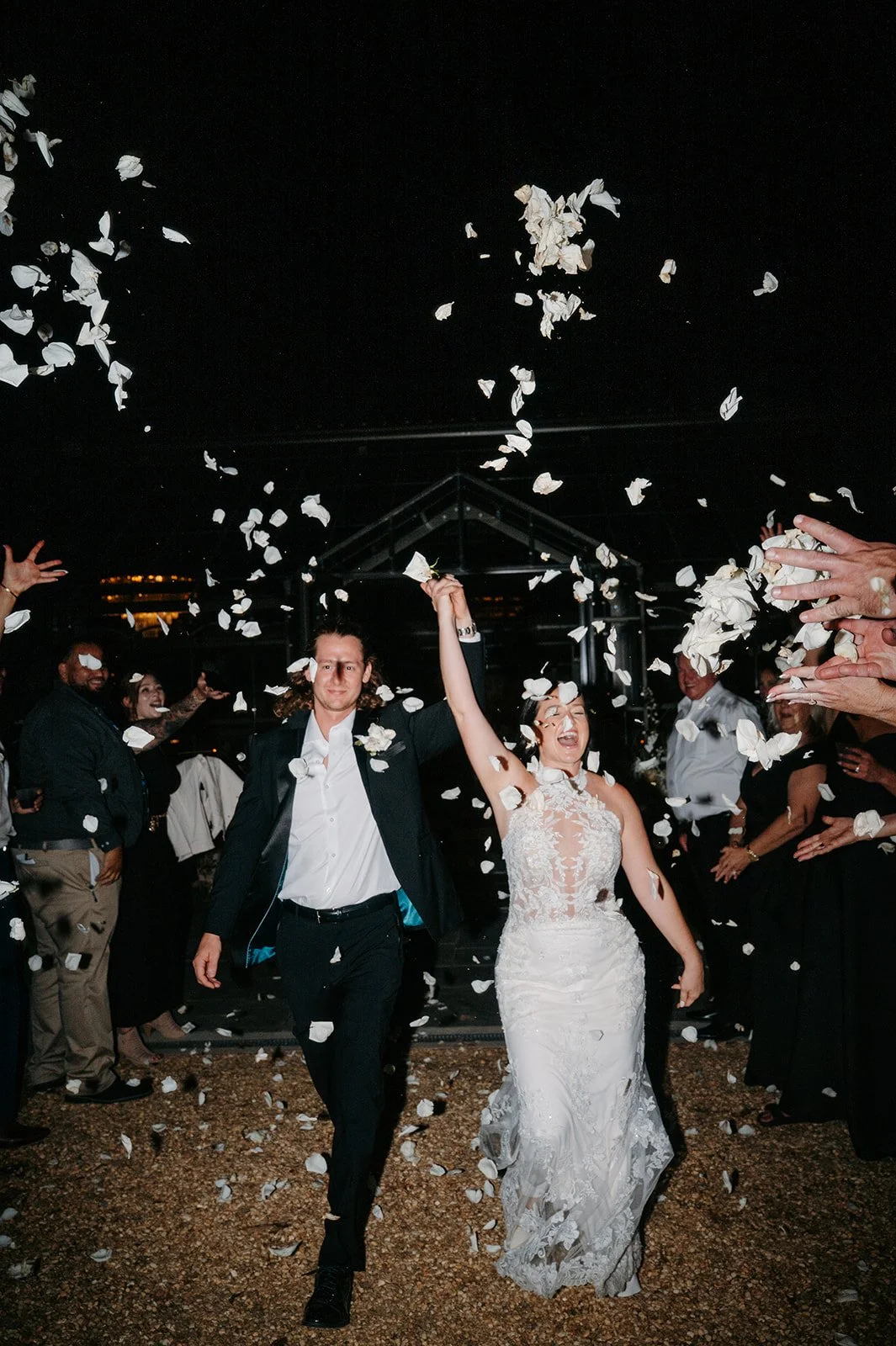 Bride and groom celebrating at their wedding with guests throwing flower petals.