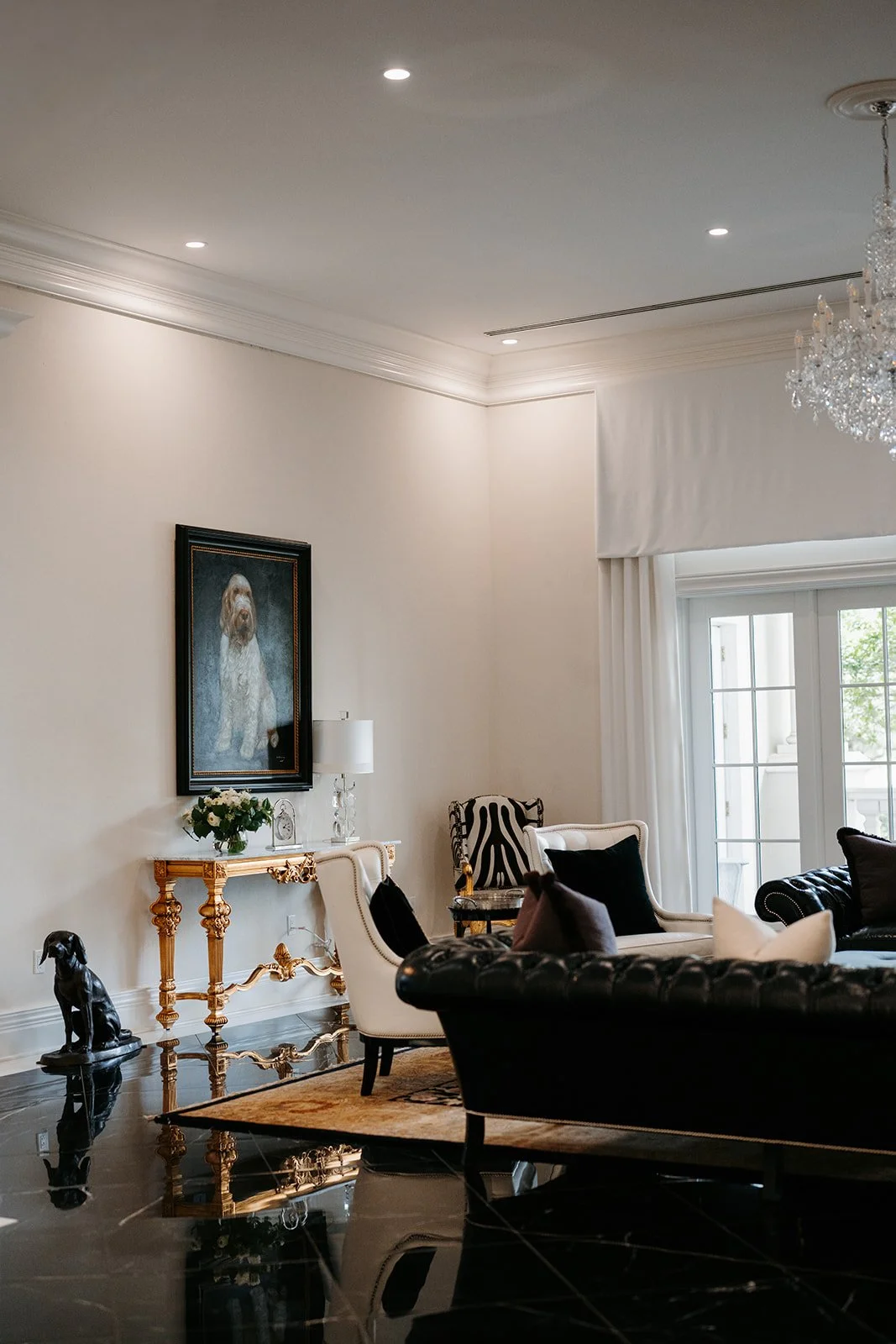 Elegant living room with black and white furniture, a chandelier, a large window, and artwork of a dog on the wall.