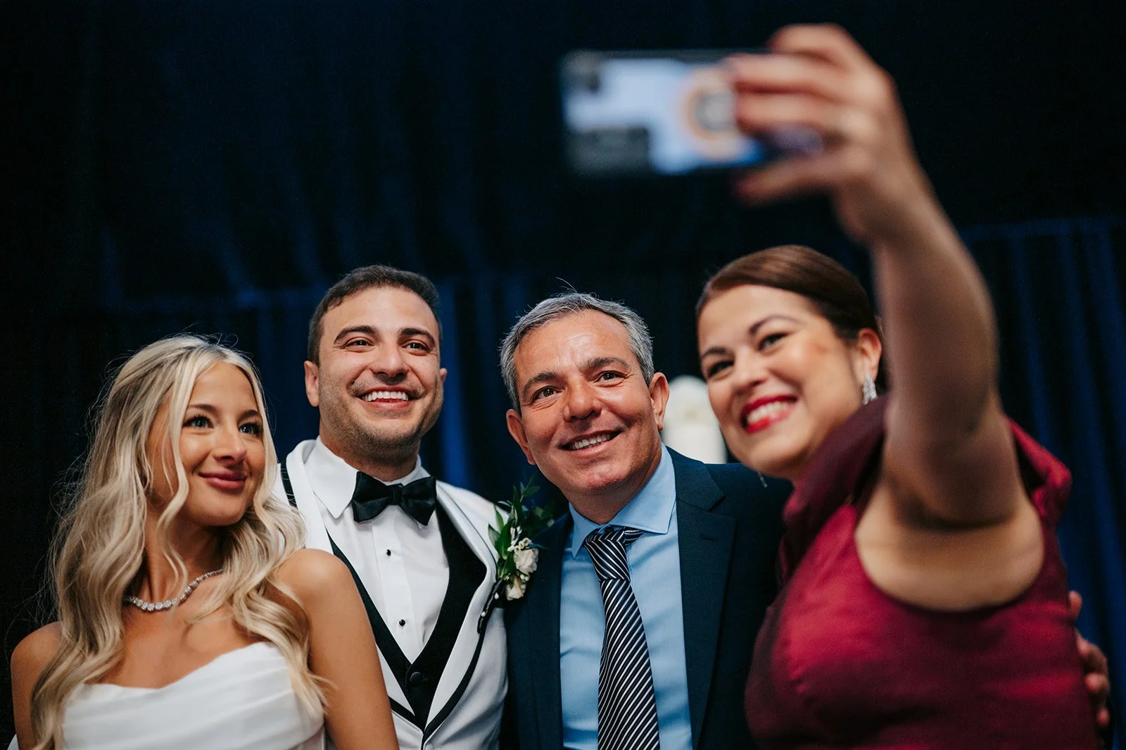 Group of four people at a wedding taking a selfie, with two women and two men dressed in formal attire, smiling and standing close together.
