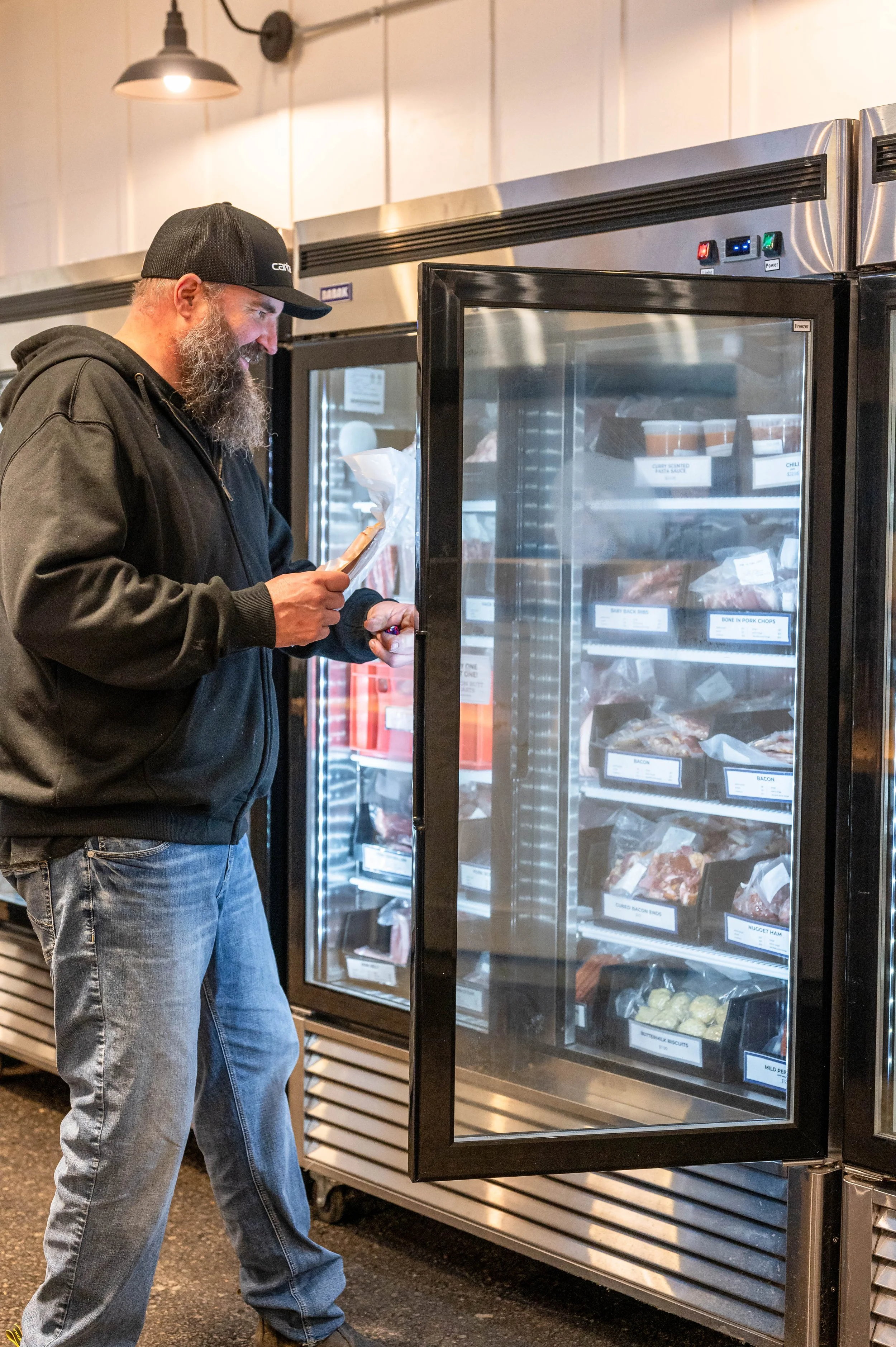 A man standing in front of a glass front freezer taking meat out of it.