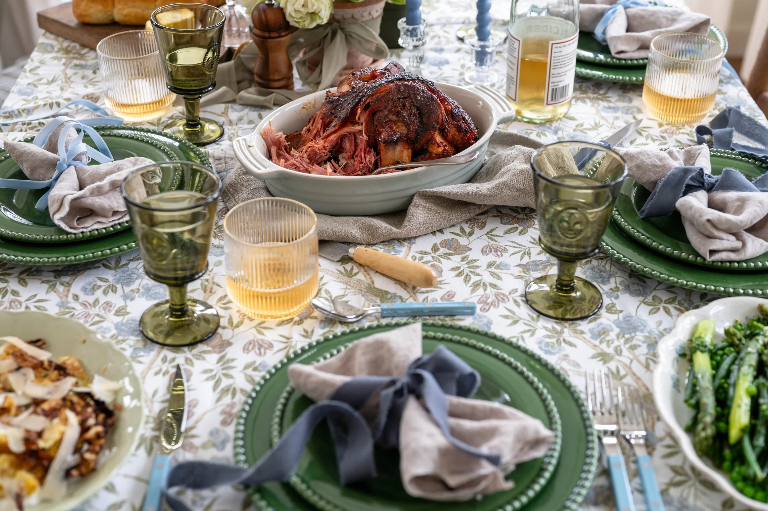 An Easter table scape covered in an easter dinner featuring bright green dishes and a glazed ham in the centre of the table