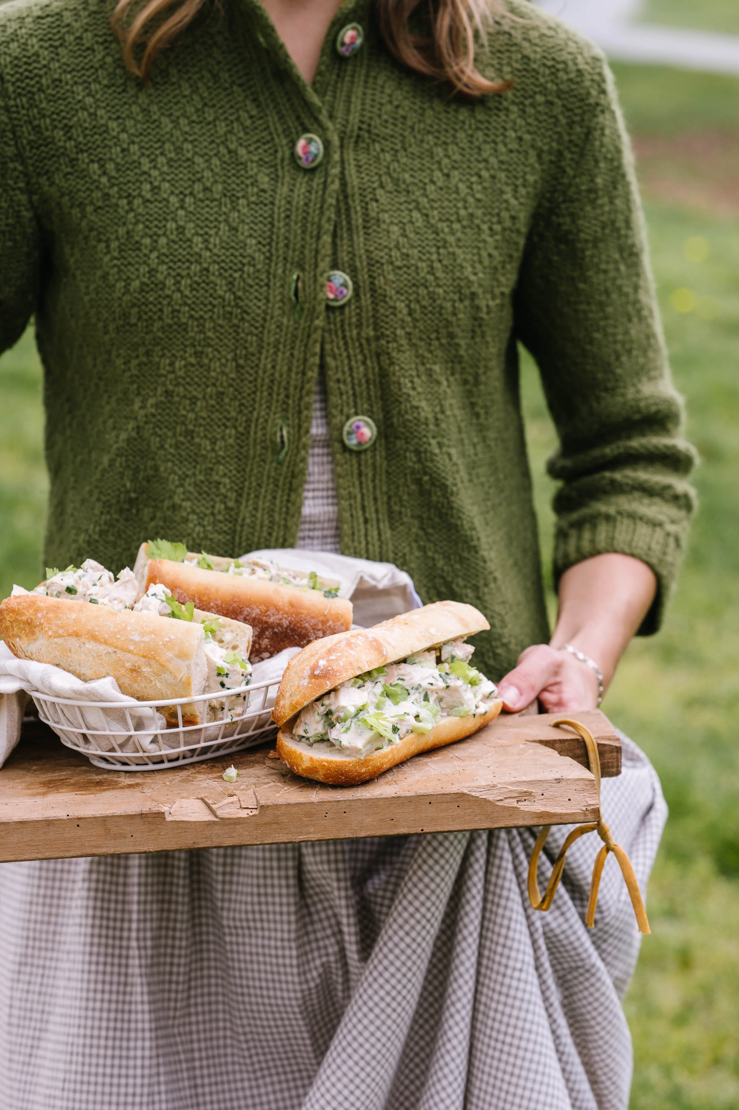 A woman holding a cutting board with chicken salad sandwiches on it