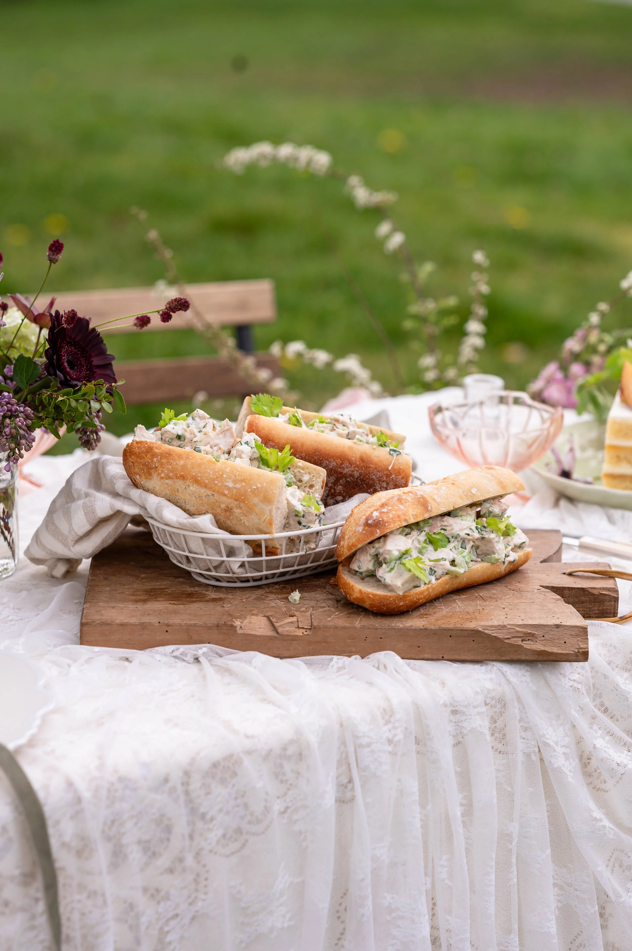 A basket of chicken salad sandwiches on a table set for Mothers Day with lace and flowers