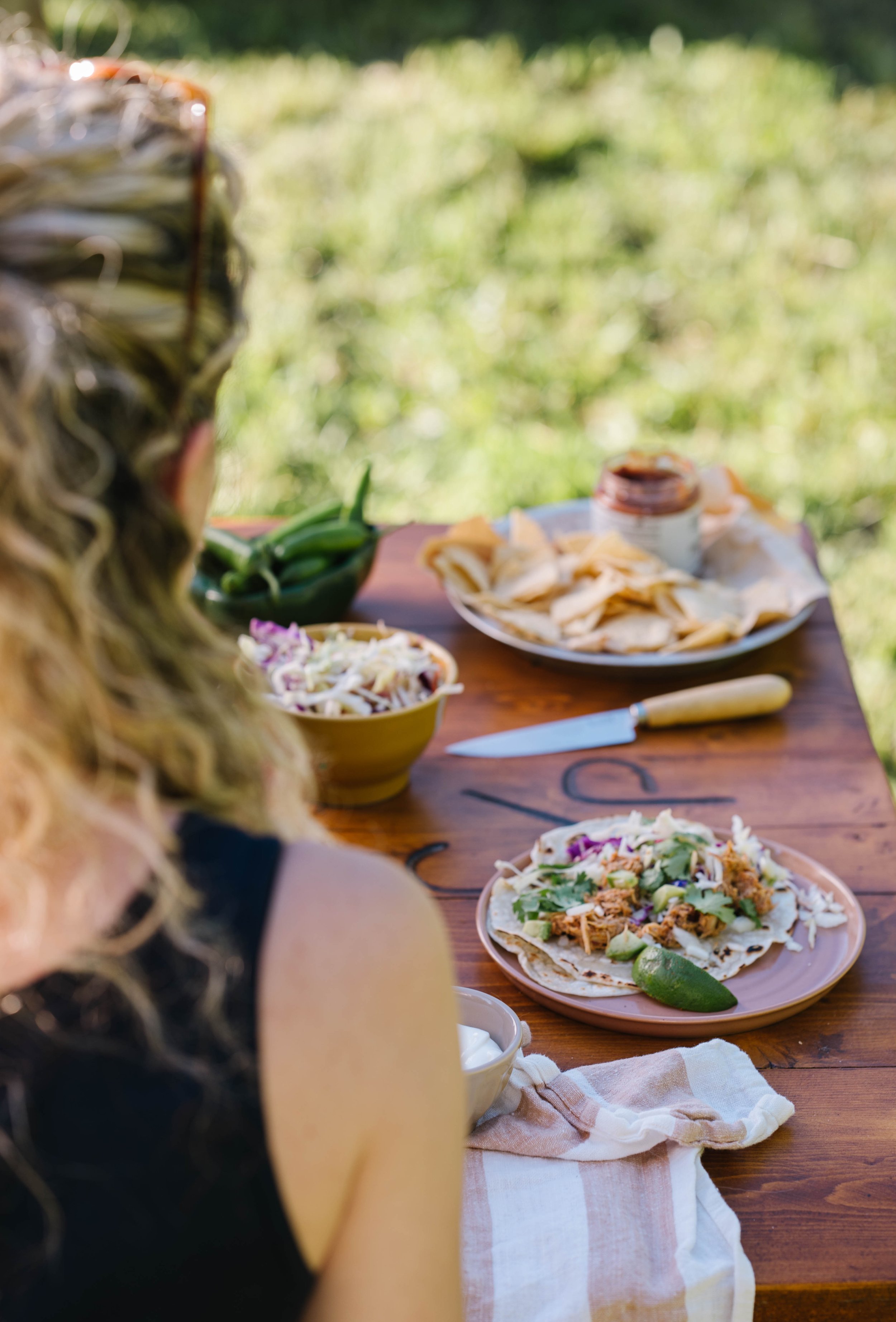 A woman sitting at the picnic table set for taco night