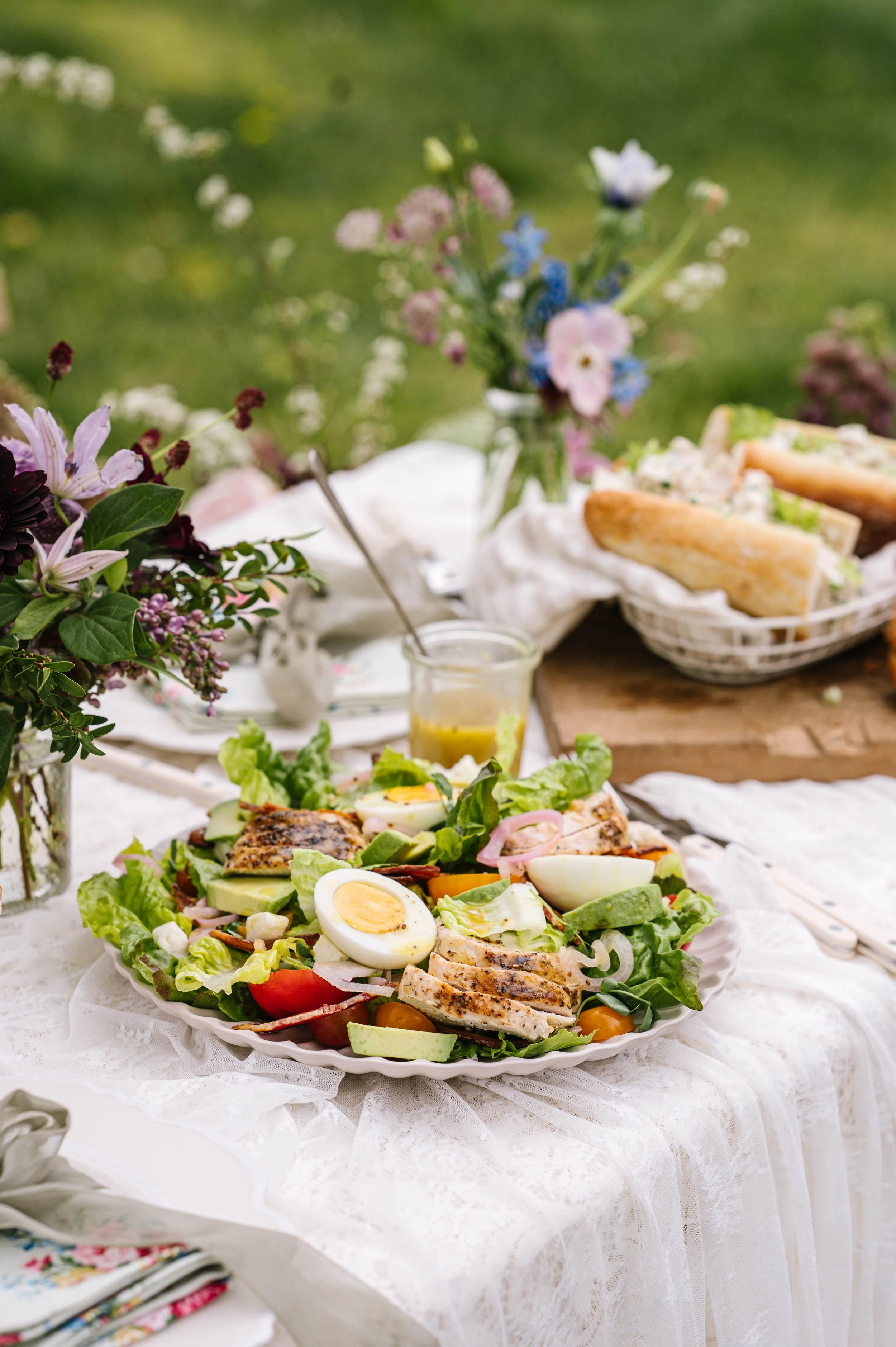 A beautiful cobb salad on a table that's dressed up for Mother's Day with lace and flowers
