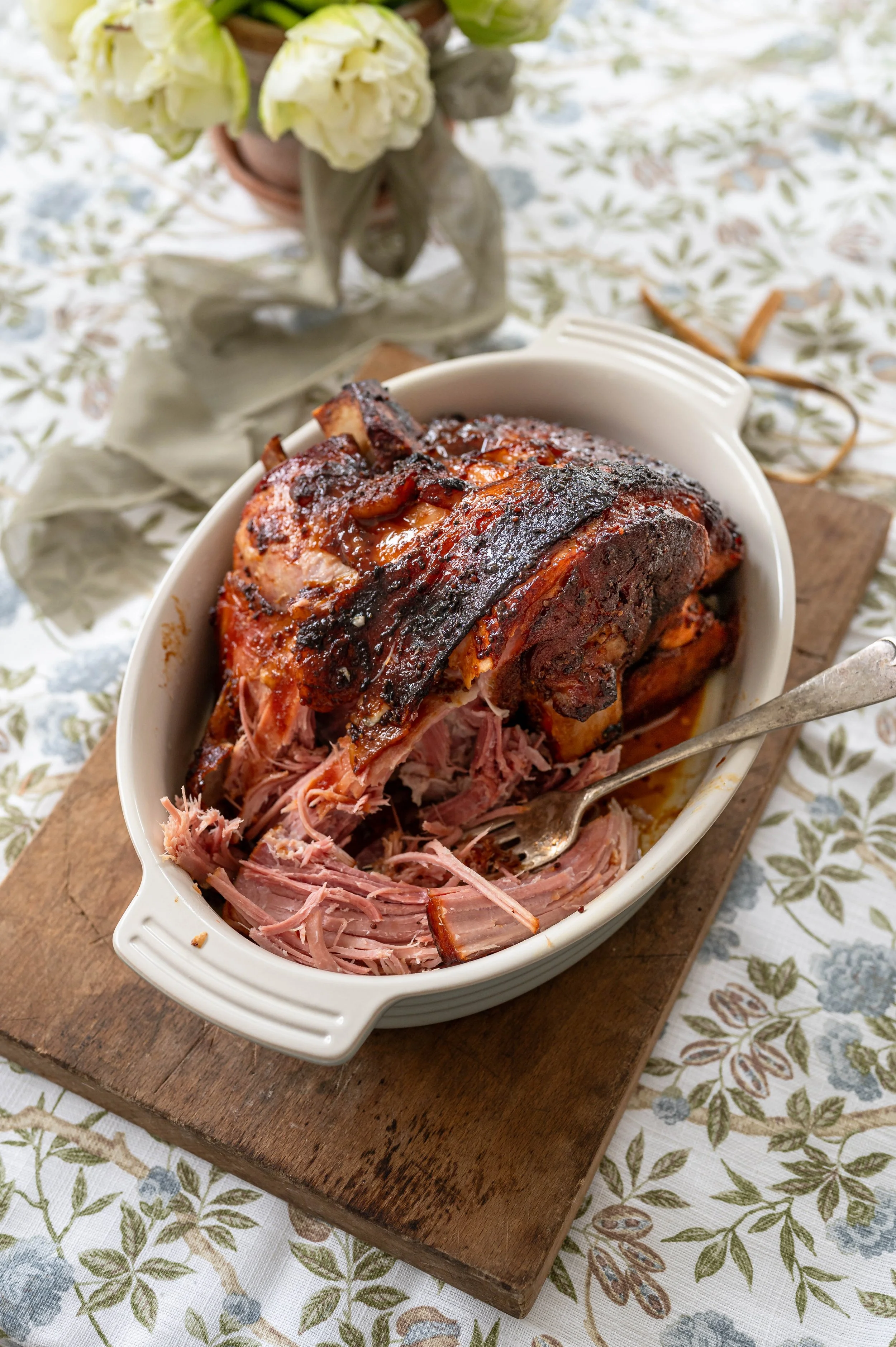 A close up of a pulled ham in a white dish on a spring floral table cloth