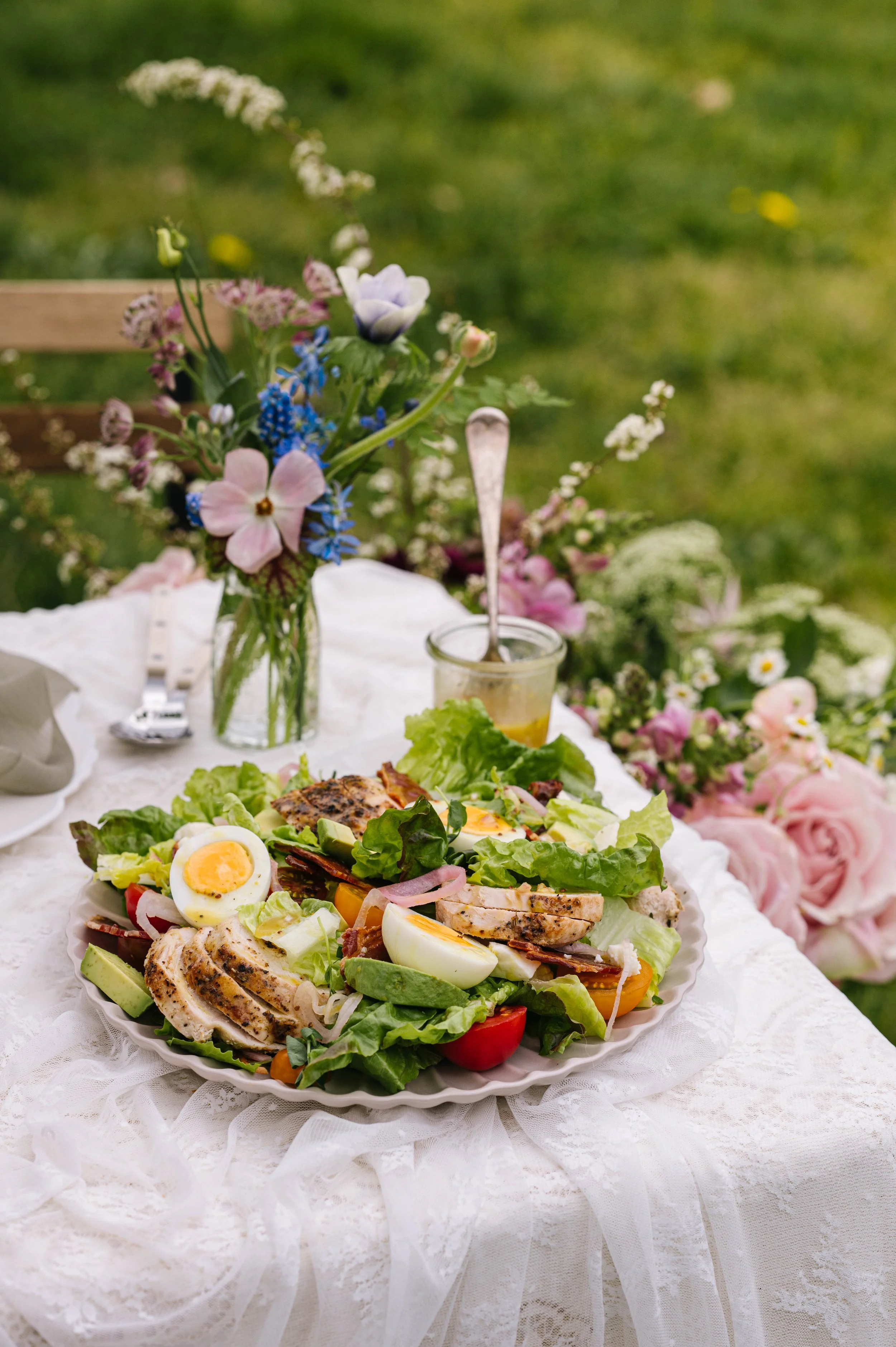 Cobb salad on a lace table cloth with flowers around the table.