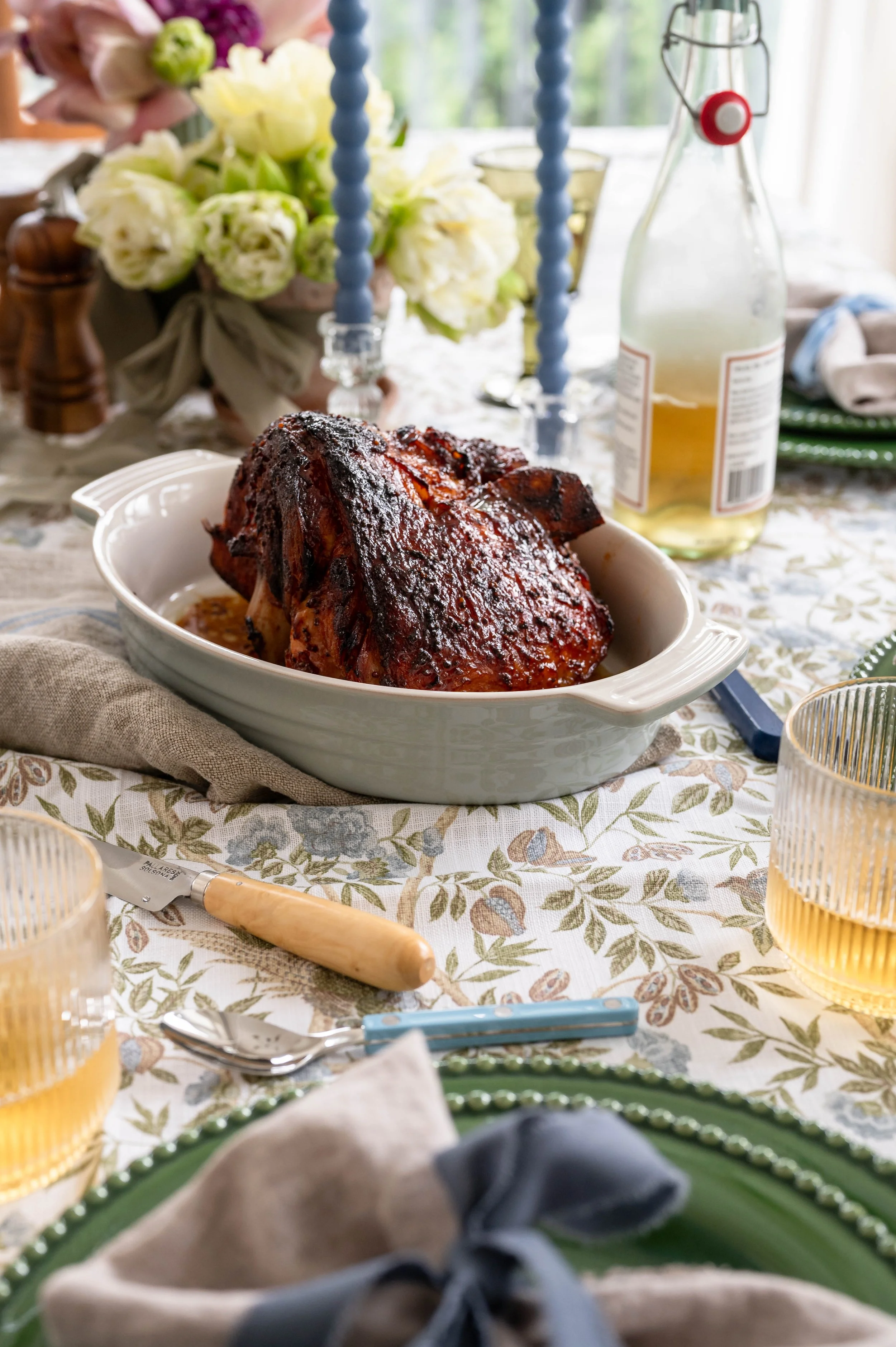 A close up of a glazed ham on a table set for Easter
