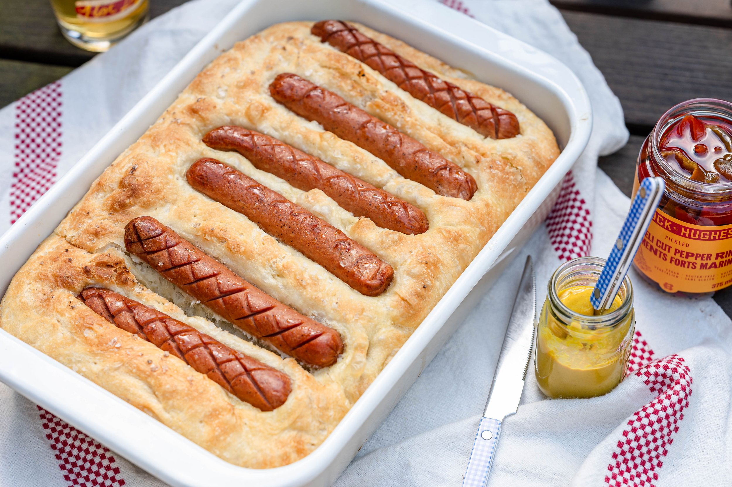 A white dish with focaccia that have hot dogs cooked into it