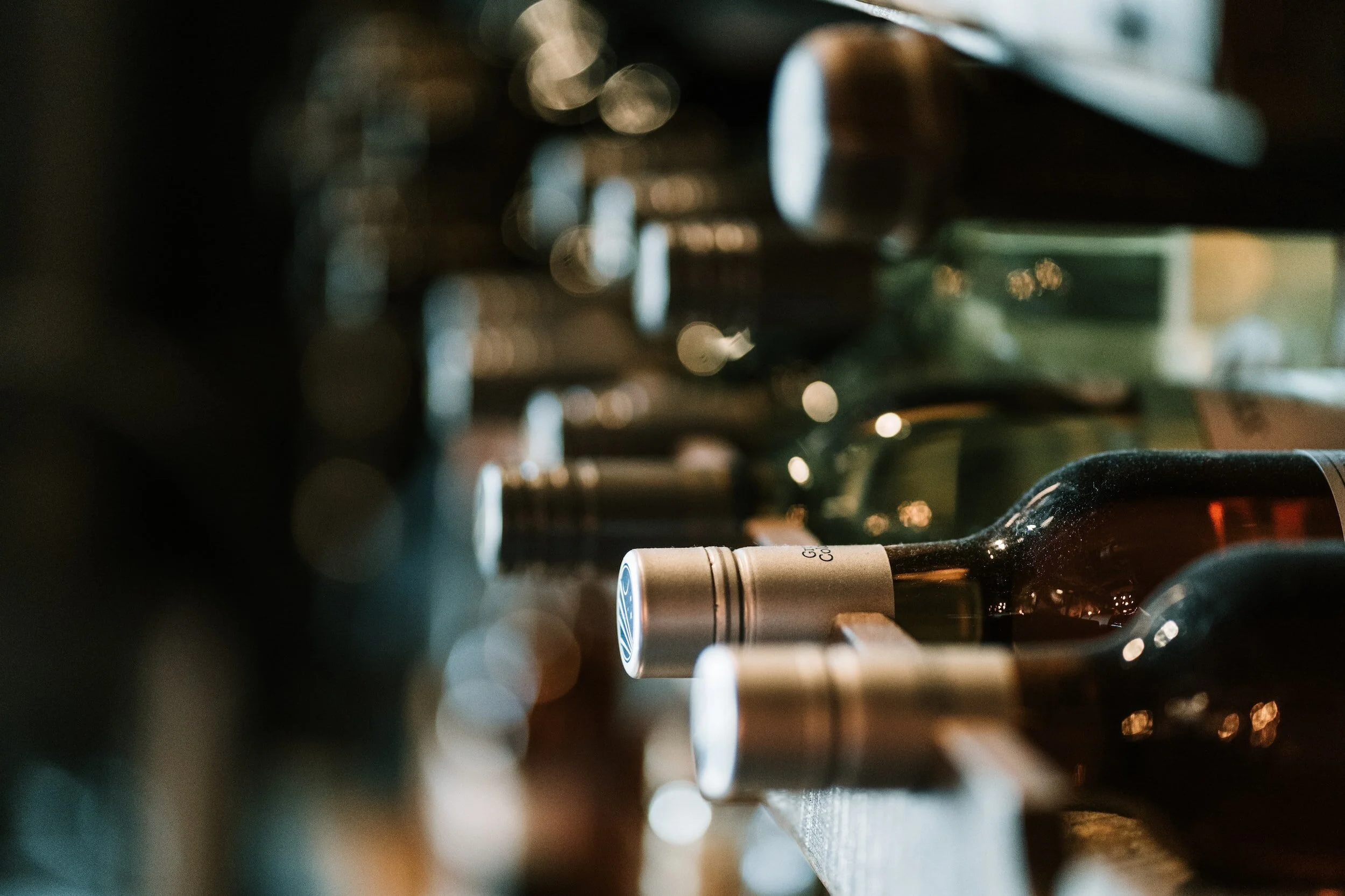 A close-up of a wine bottle among other bottles in a dimly lit setting, with a bokeh effect creating blurred circular light spots.