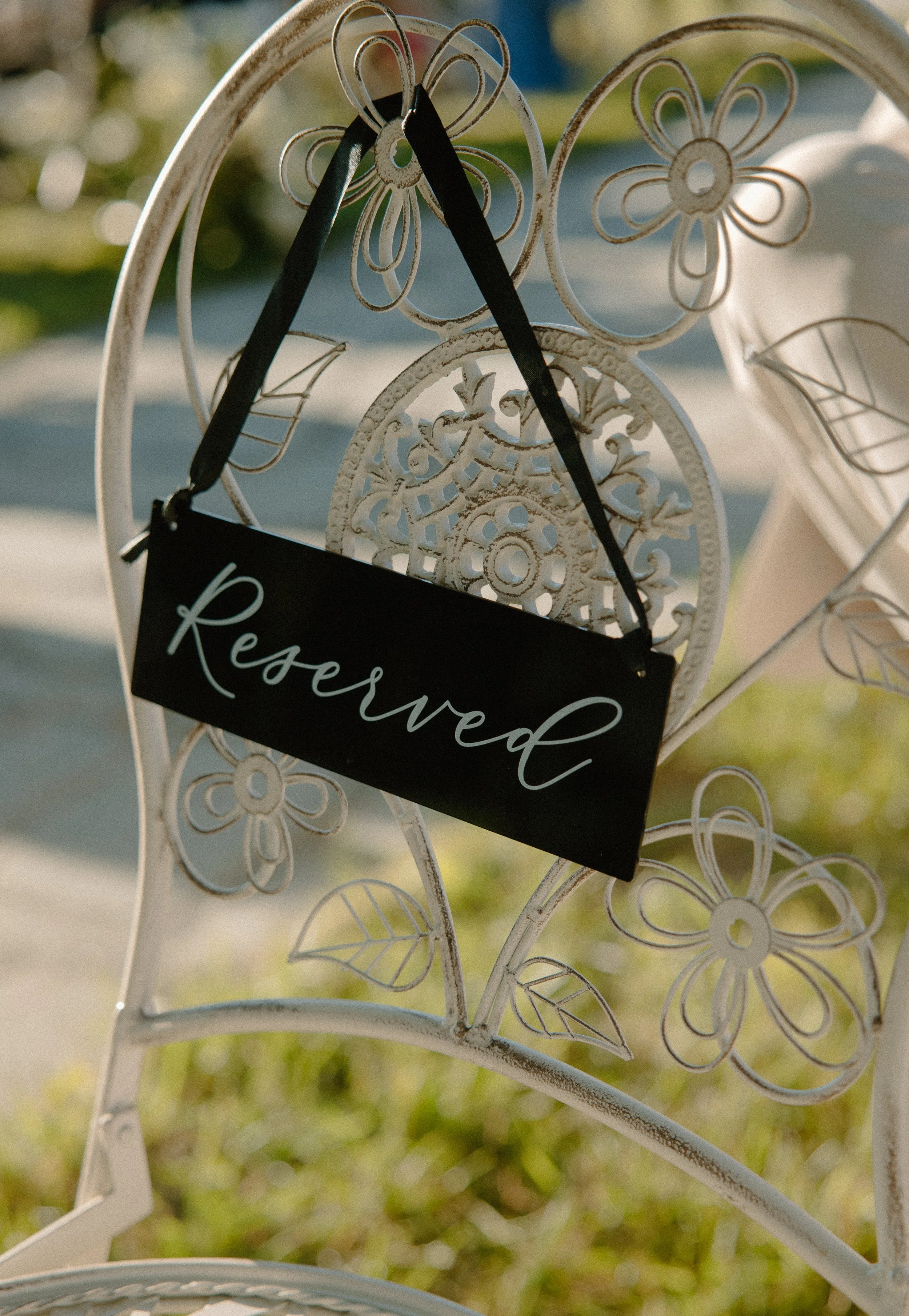 White decorative metal stand with flower and leaf patterns, holding a black sign with the word 'Reserved' written in white script.