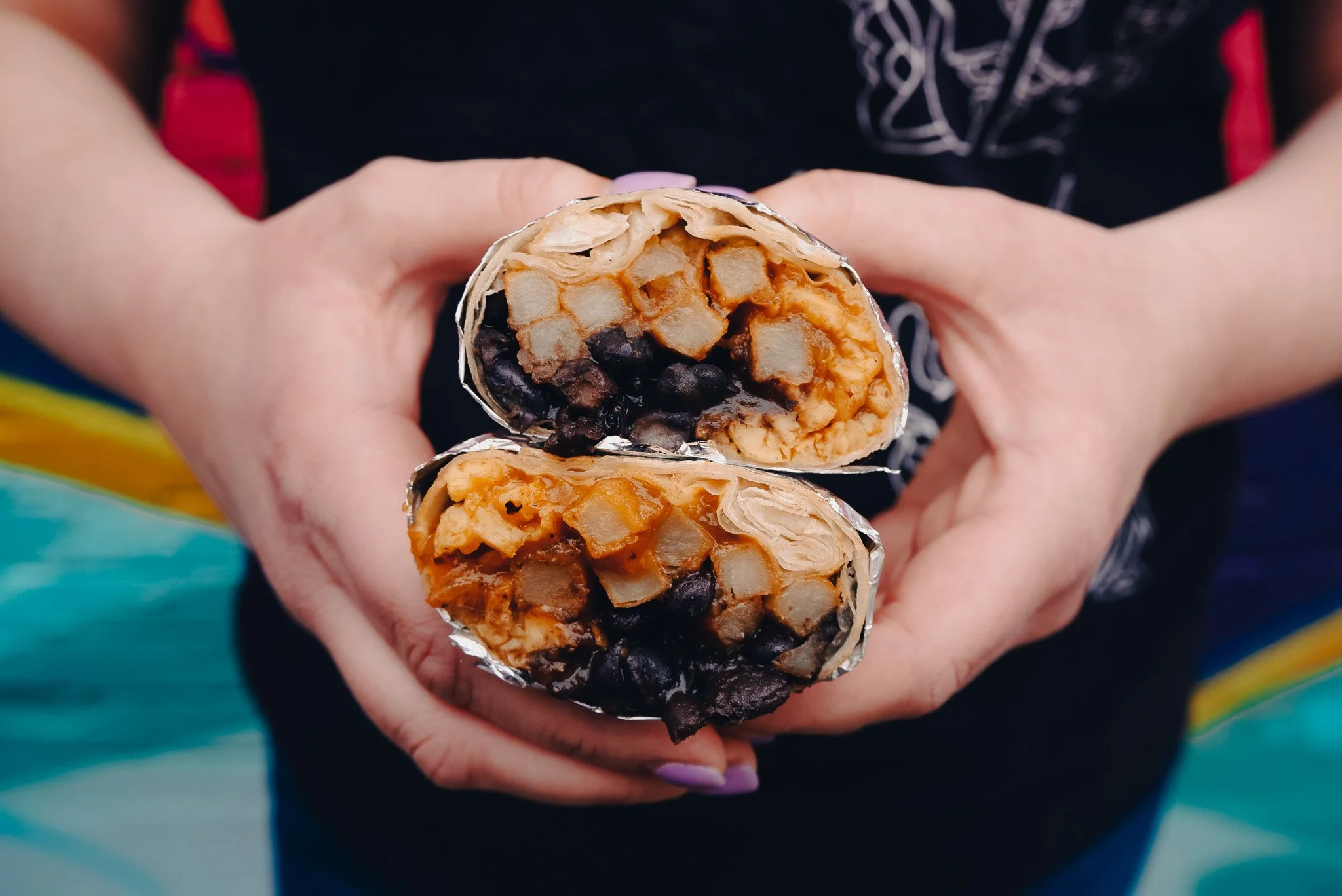 A person holding two halves of a breakfast burrito that has fries and black beans.