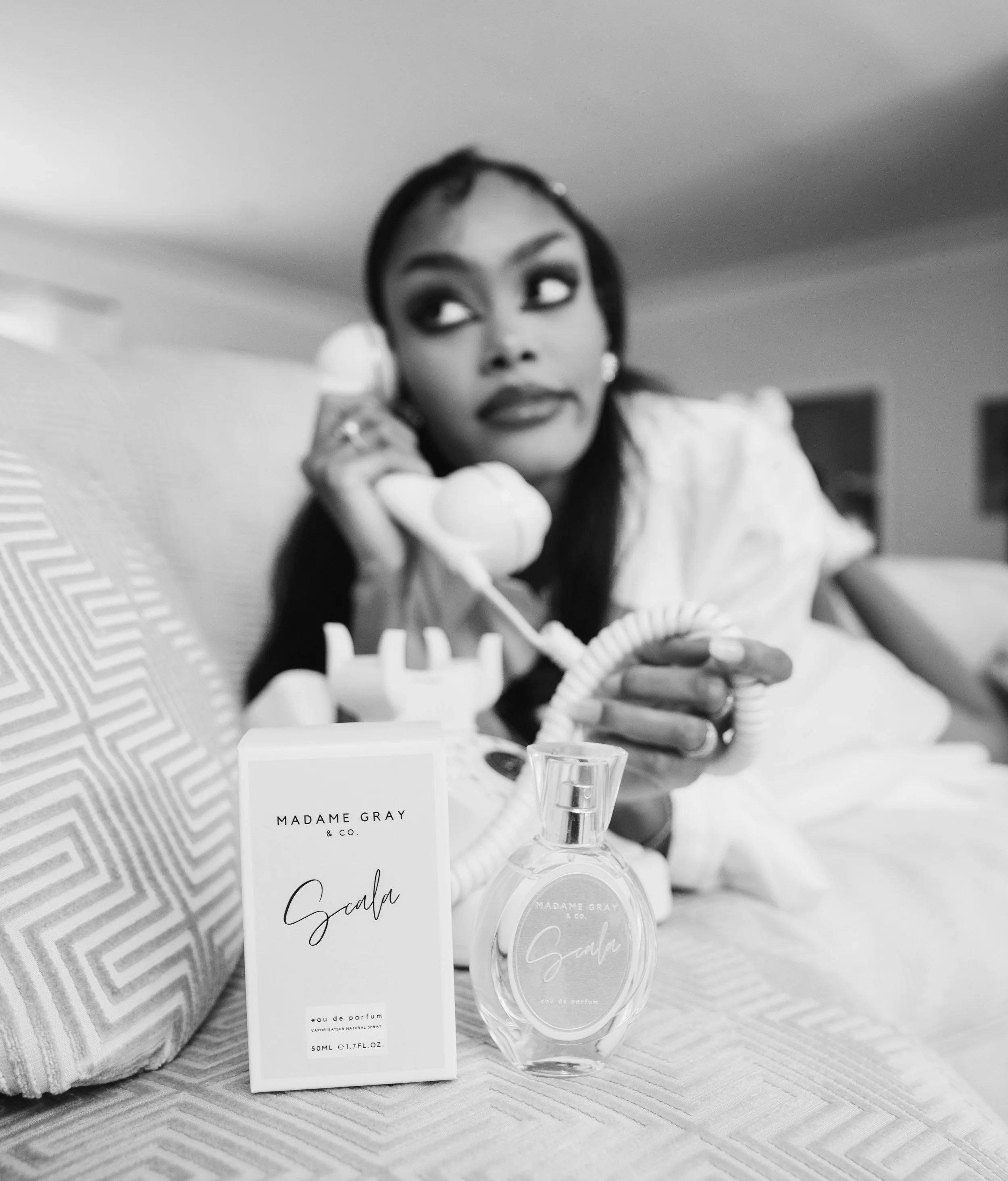 Black and white photo of opera singer and voice actor, Randall Gray, with her fragrance, "Scala," from her luxury goods brand, "Madame Gray & Co.".