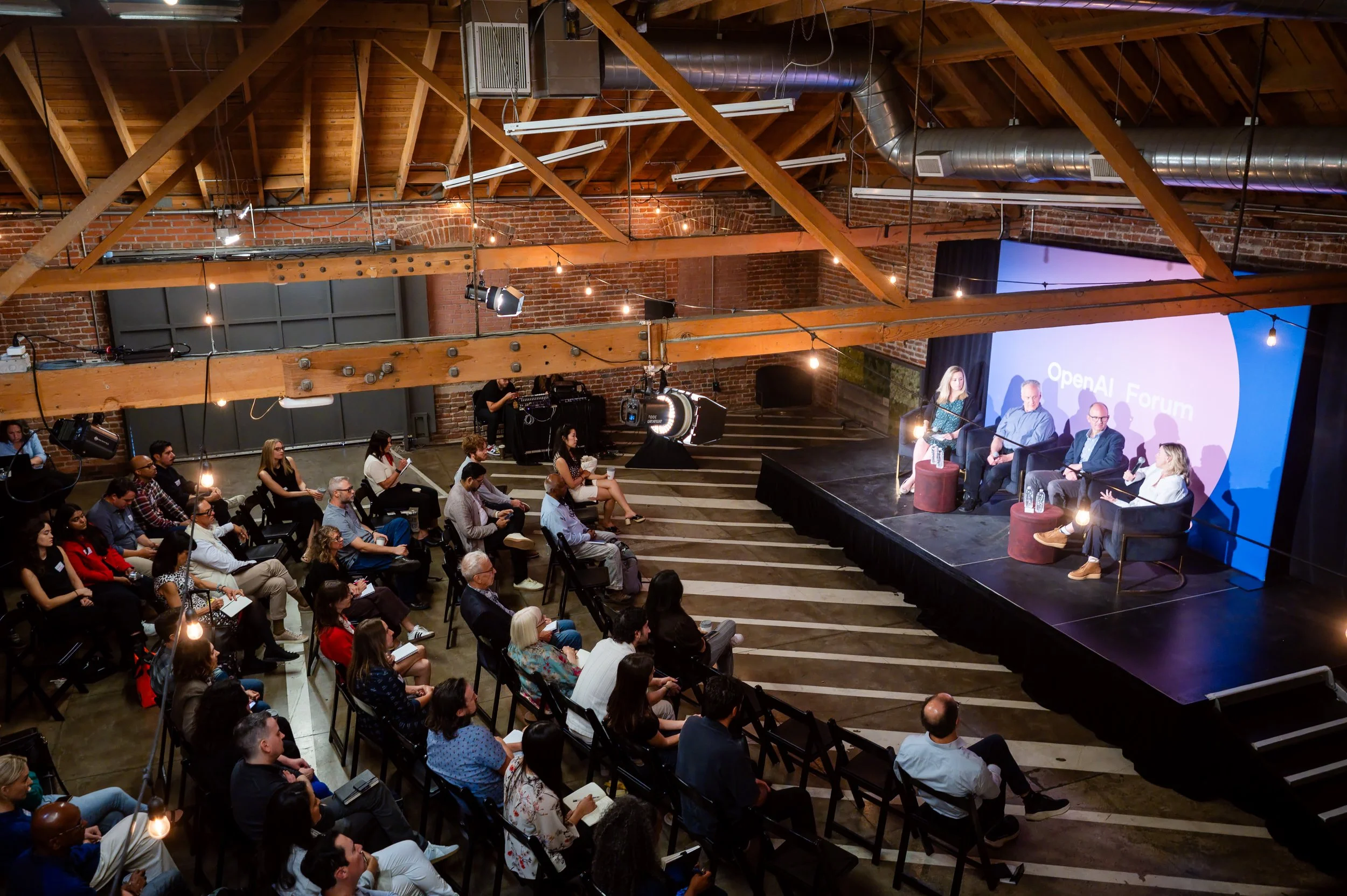 A packed room watches Olivia Smith moderate an OpenAI Forum panel on how local newsrooms are using AI