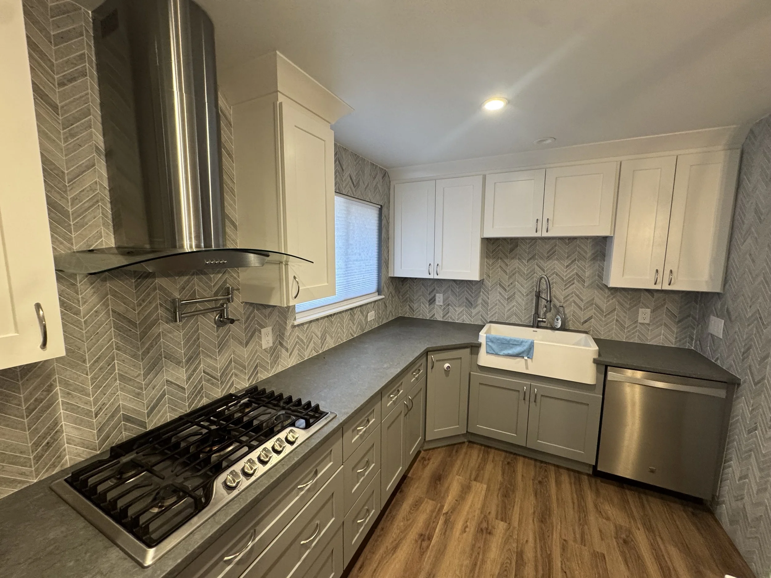 Gray kitchen countertops with a farmhouse sink and chevron tile backsplash.