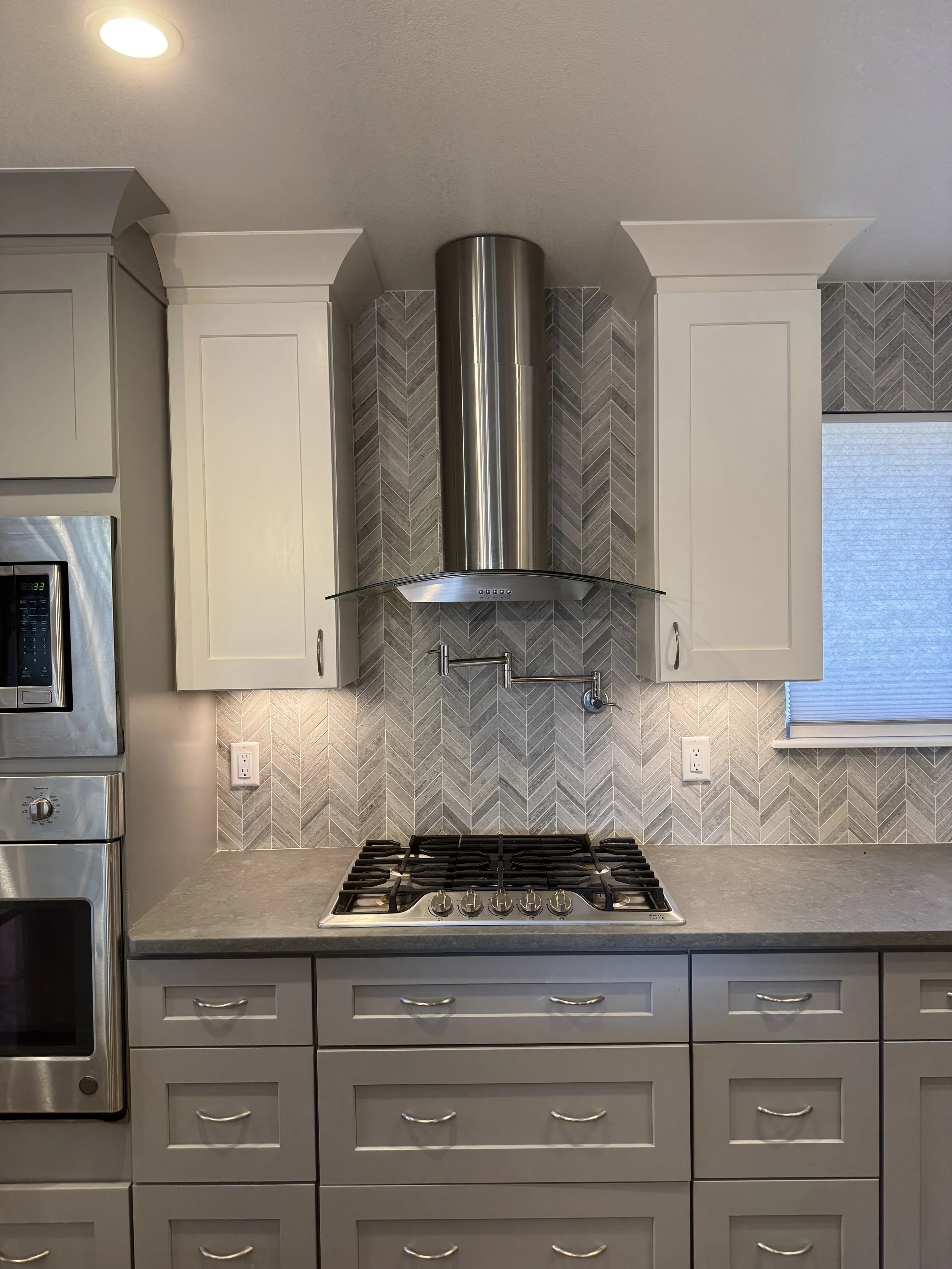 Kitchen countertop detail surrounding a gas cooktop with a chevron tile backsplash.