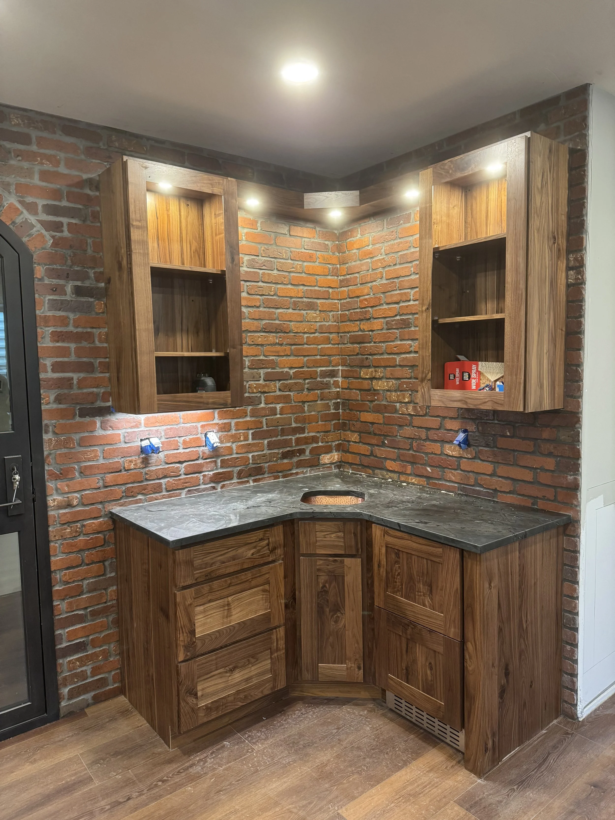 Dark corner countertop installation with a copper sink, wood cabinets and brick backsplash.