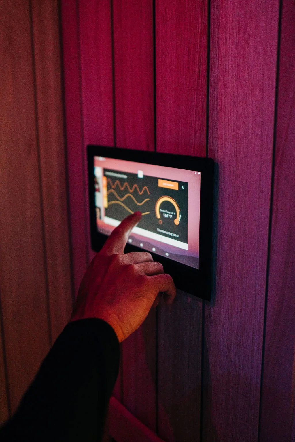 A person touching a digital thermostat or control panel on a wooden wall, displaying temperature and energy data.