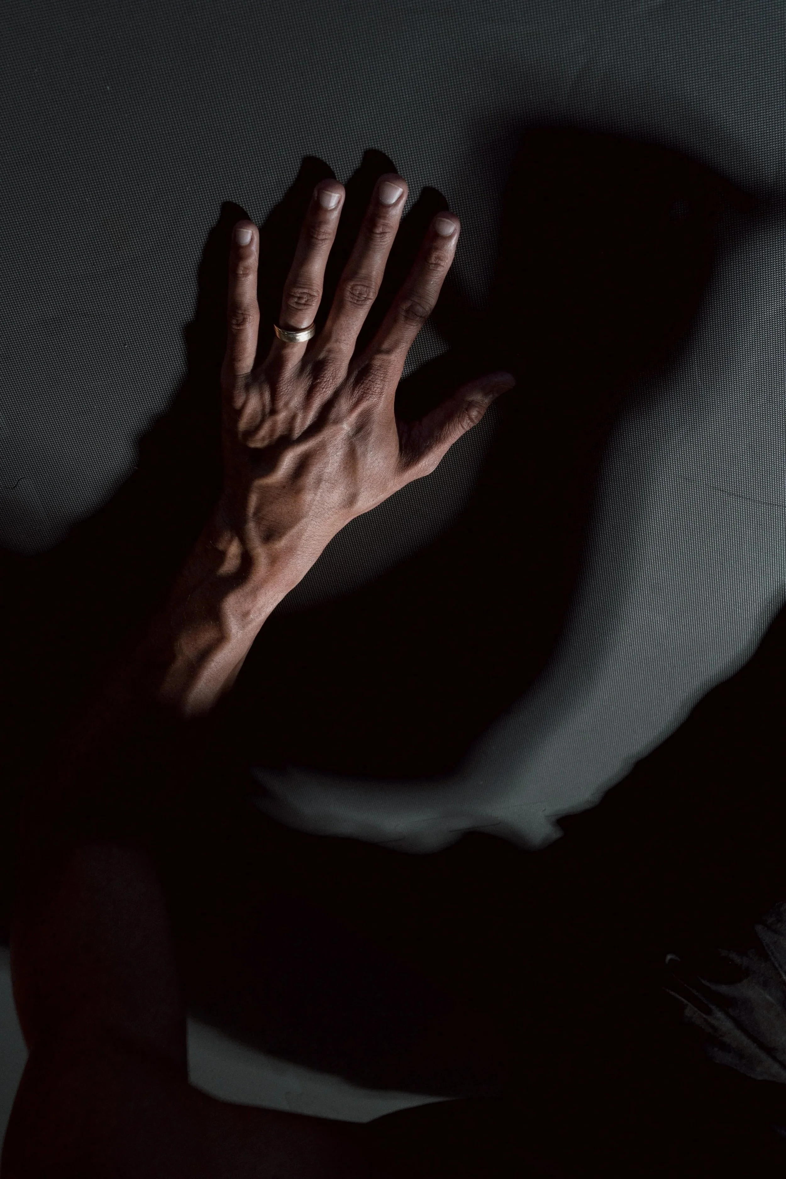 A person's hand with a wedding band, hand pressed against a textured surface, casting a shadow.