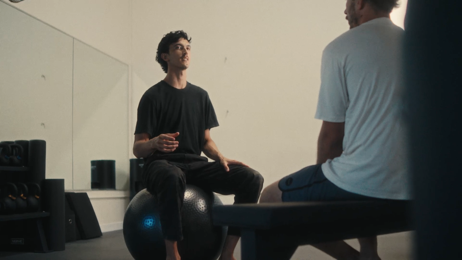 Two men in workout attire engaging in conversation during a fitness session in a gym.