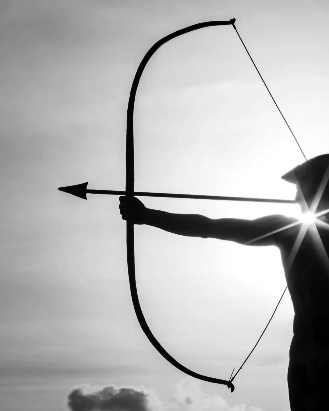 Silhouette of a person holding a bow and arrow, ready to shoot, with the sun shining behind and a cloudy sky.