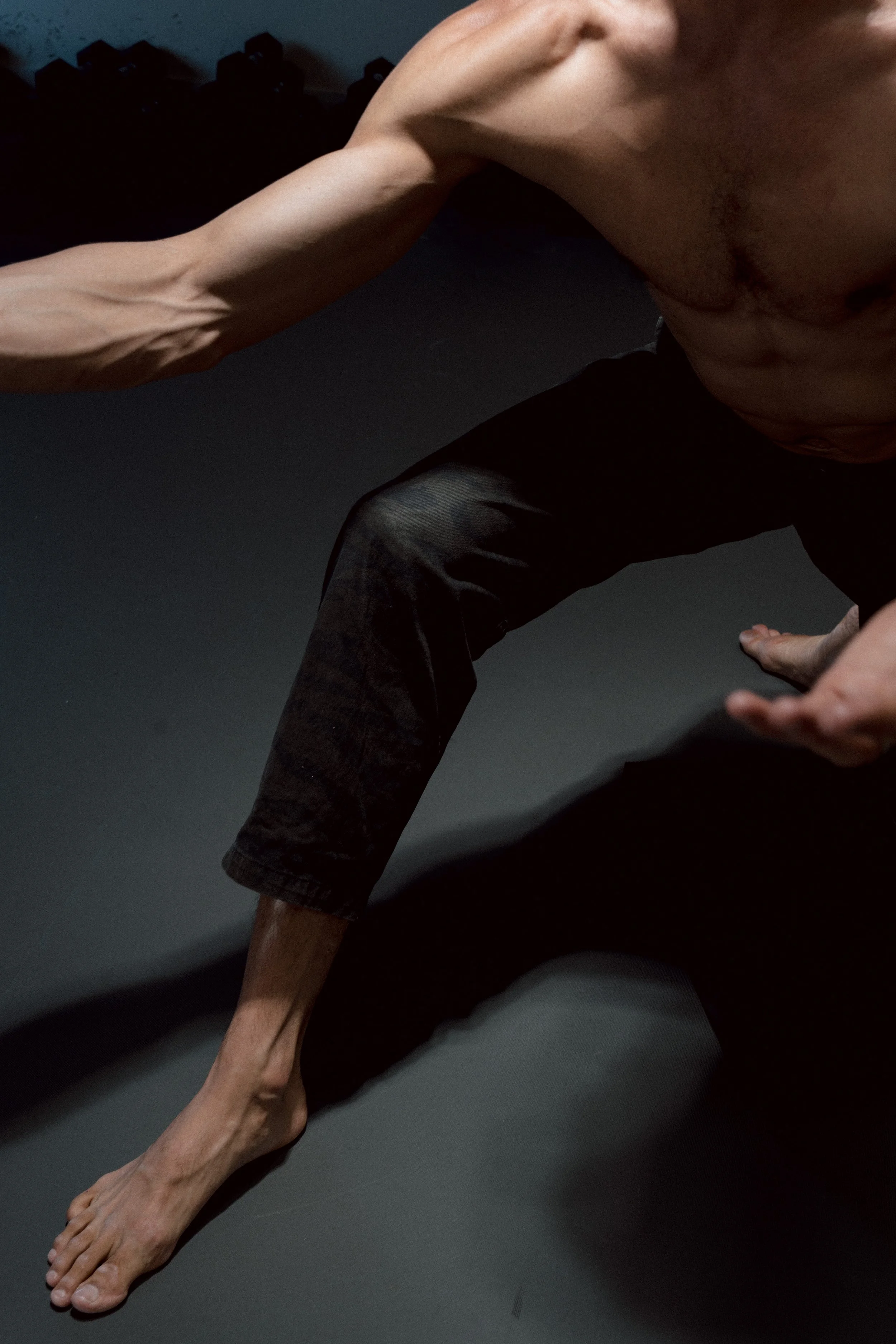 Person in a side plank yoga pose on a dark mat, with one arm extended and supporting their body, wearing black pants and no shirt.