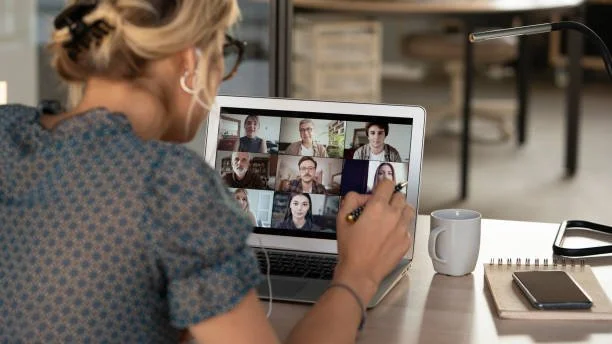 Woman participating in a virtual meeting on a tablet, with multiple people's video calls displayed.