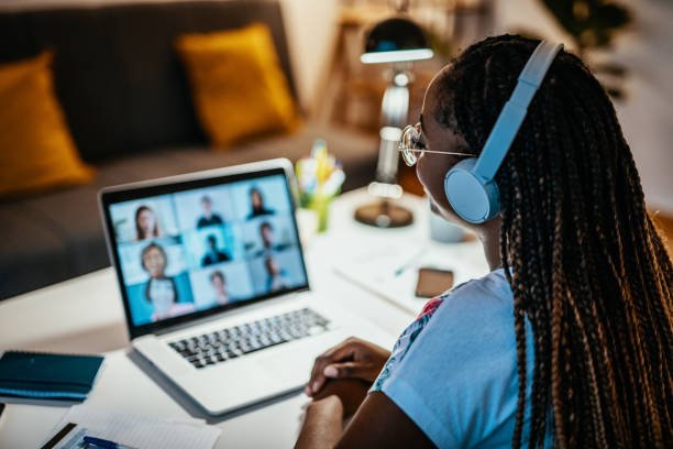 A woman wearing headphones attending a virtual meeting on her laptop, with multiple people visible on the screen.