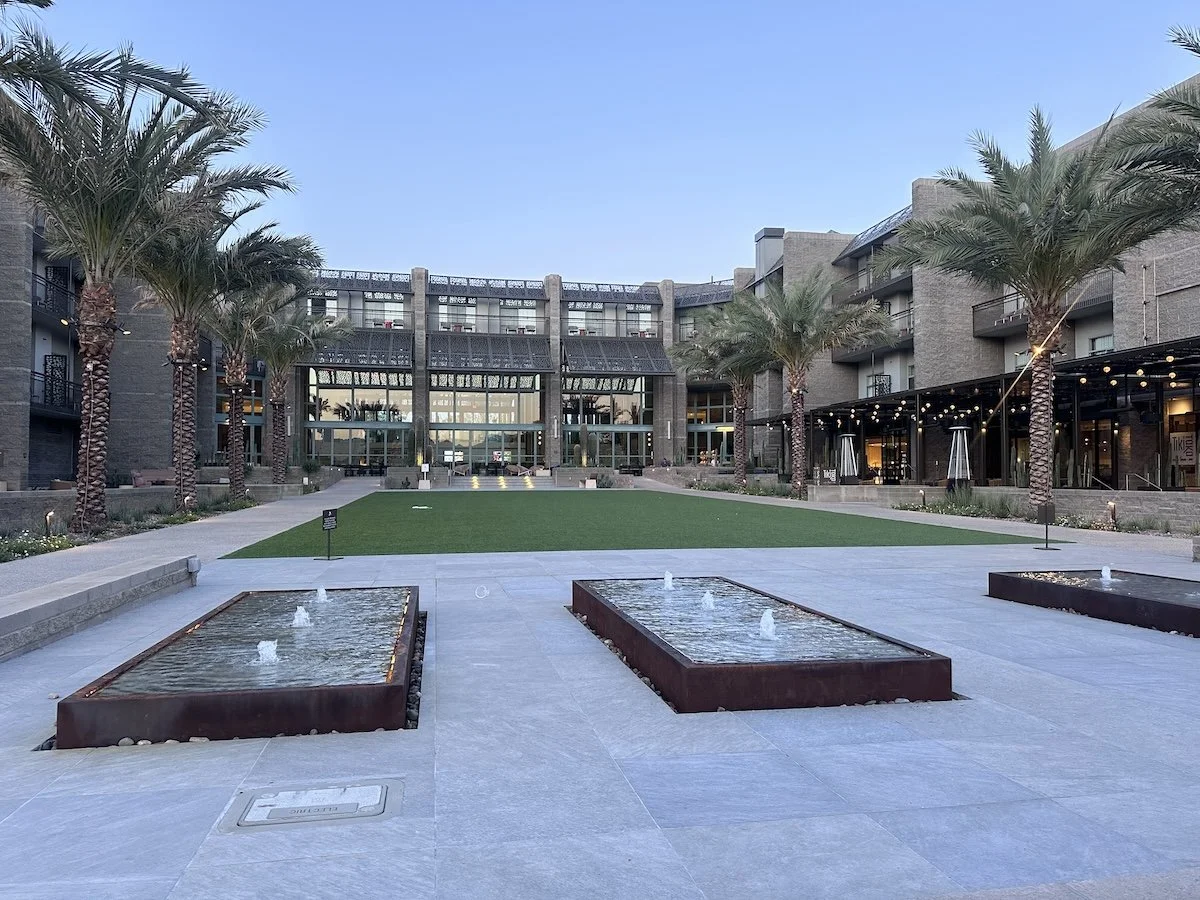 A view of the outdoor area at the Grand Hyatt Scottsdale- there are small fountains in the front and turf grass. There is also restaurant seating