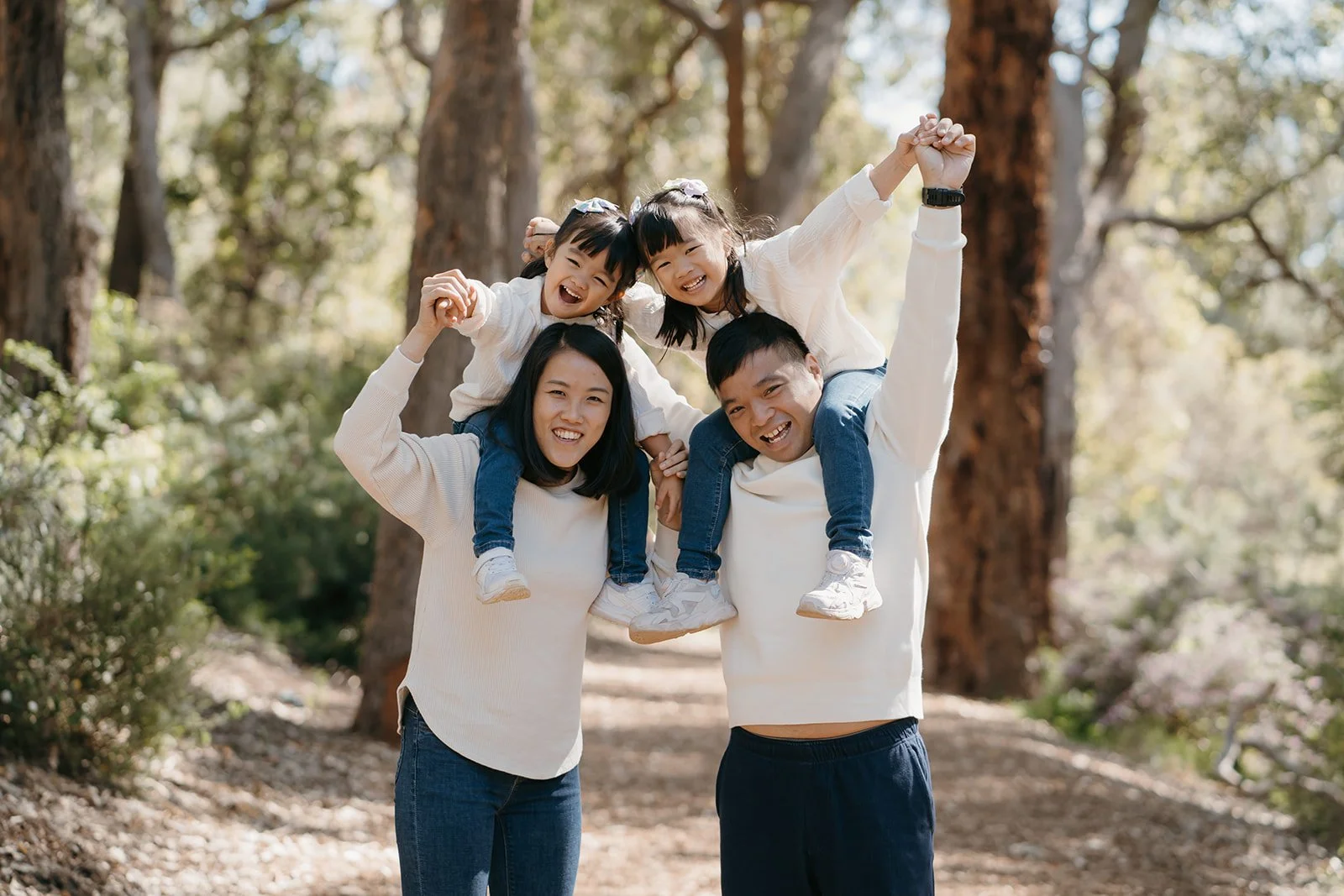 Family photoshoot of two young daughters on their mom and dad's shoulders during a trail walk in Perth