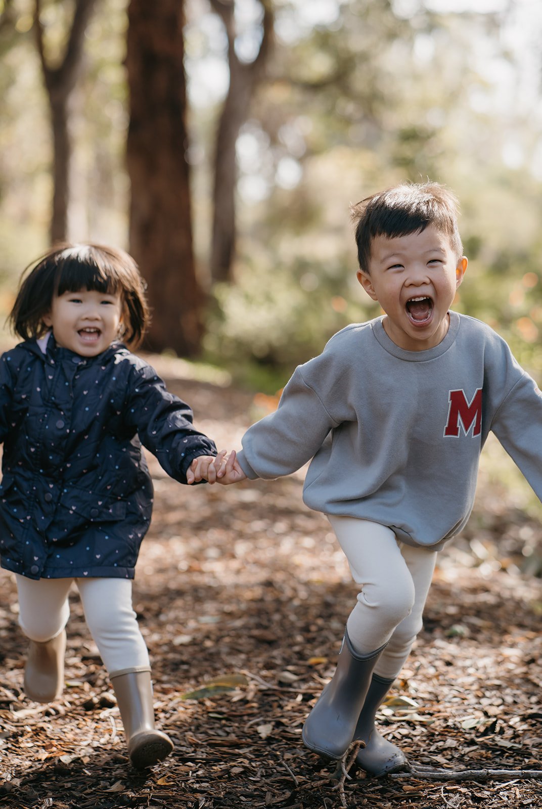 Family photoshoot of young brother and sister holding hands and running happily in the park