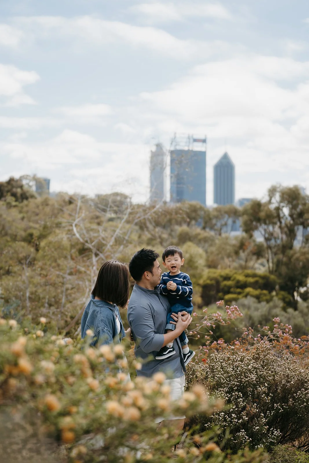 Family photoshoot of mom and dad with their toddler son walking through the wildflower trail in Perth park during spring