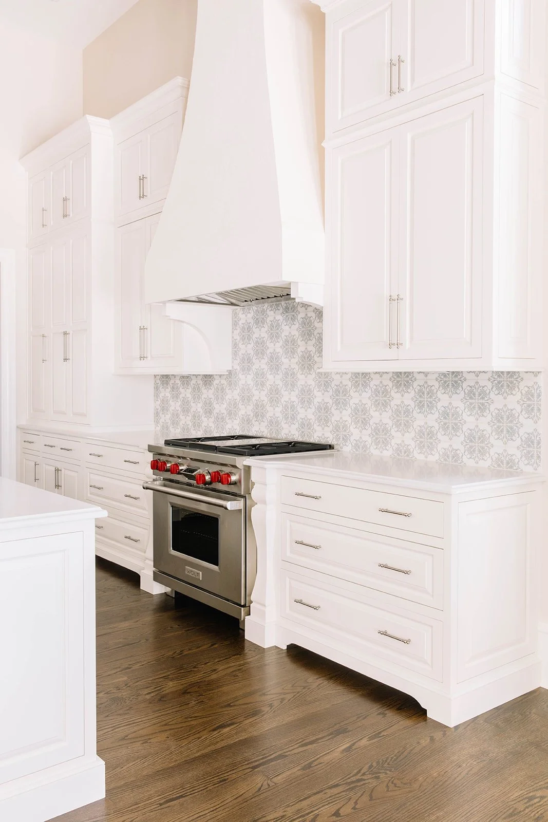traditional kitchen with white cabinets, decorative hood and patterned backsplash.