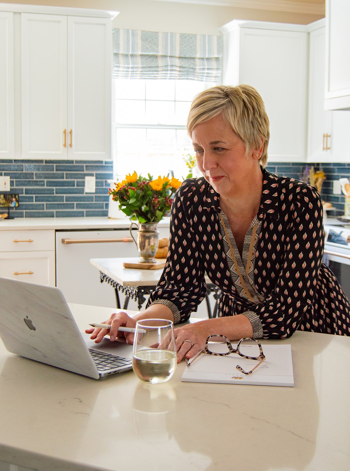 woman leans over kitchen counter at laptop