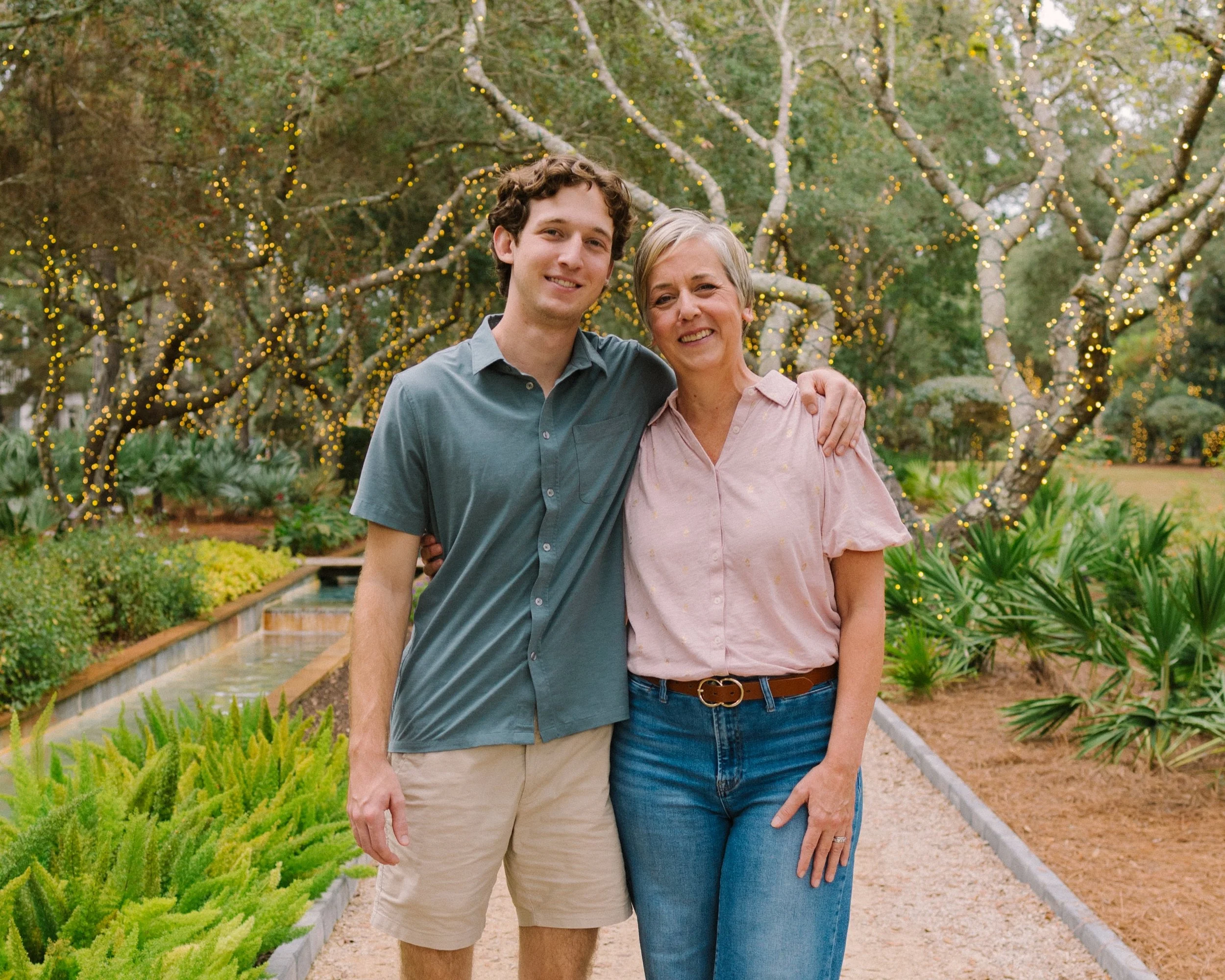 a photo of mother and son posed outside under trees with lights