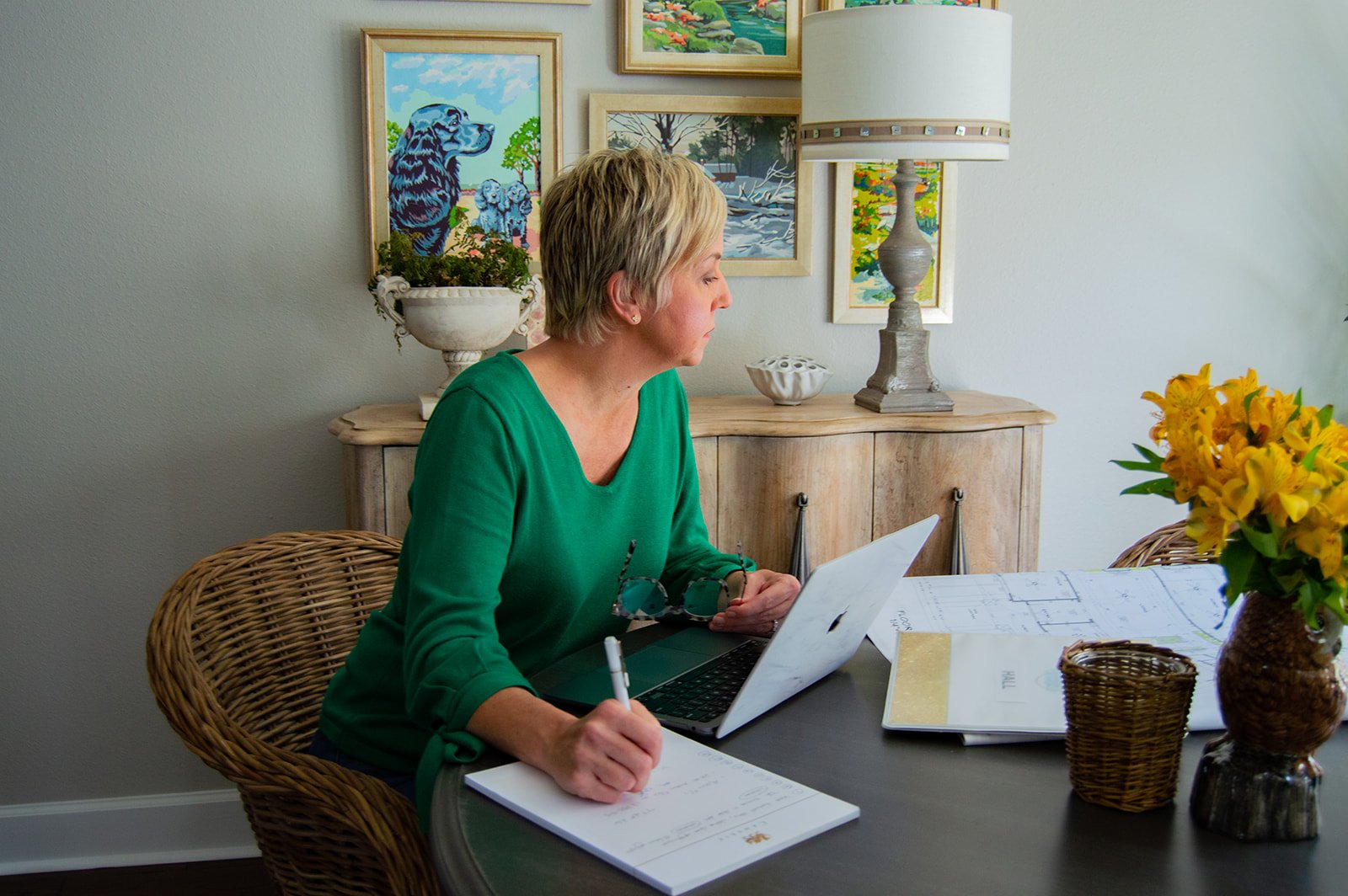 woman in green shirt works at table with laptop and house plans