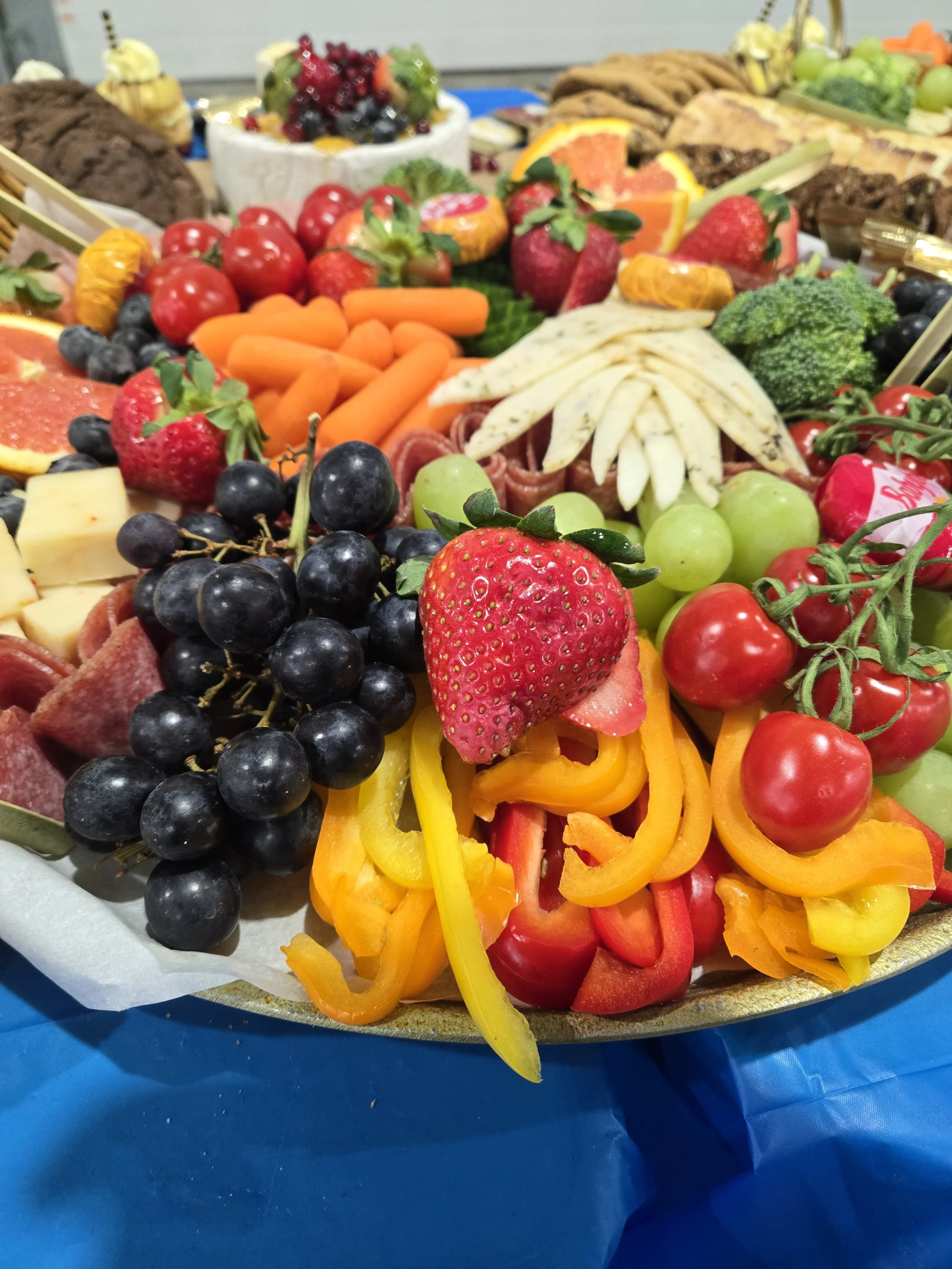 Colorful display of fresh fruits and vegetables including strawberries, grapes, cherry tomatoes, bell peppers, carrots, broccoli, and cheese, arranged on a platter.