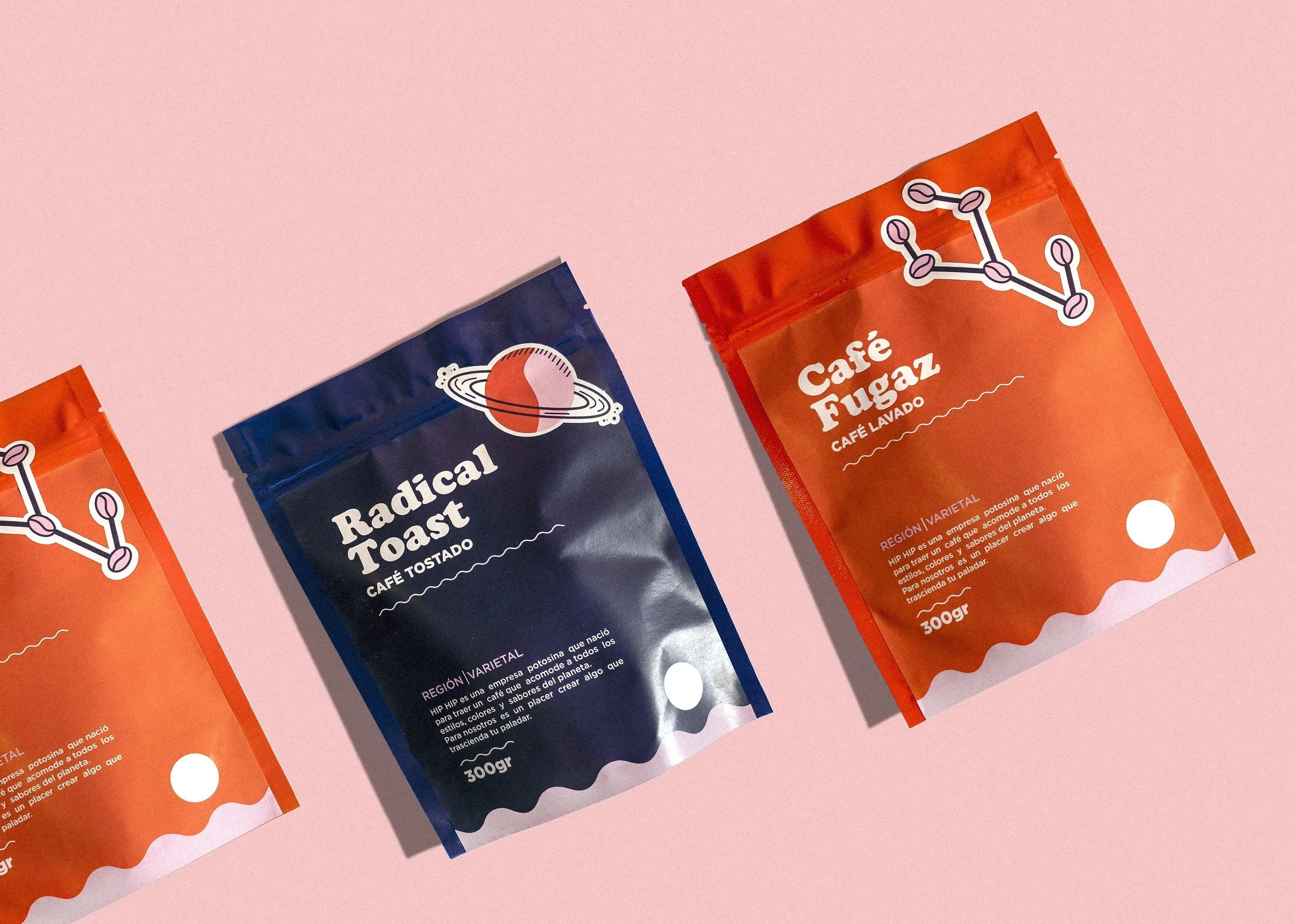 Three coffee packets on a pink background, with two orange packets on either side and a dark blue packet in the middle. The packets have labels indicating different coffee blends.
