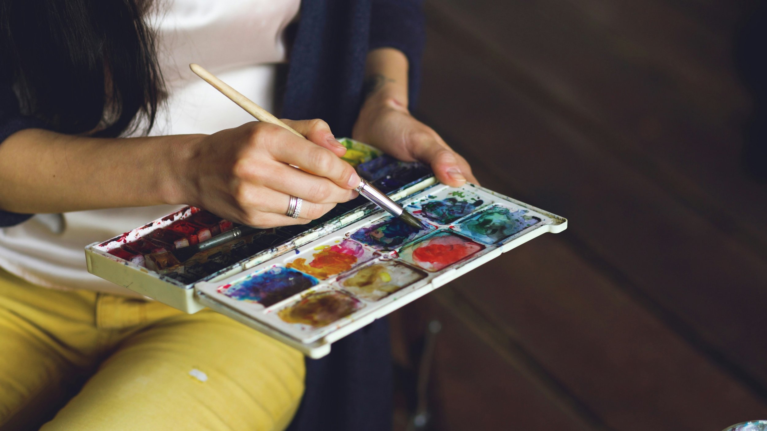 An artist mixing watercolour paint on a palette with a brush