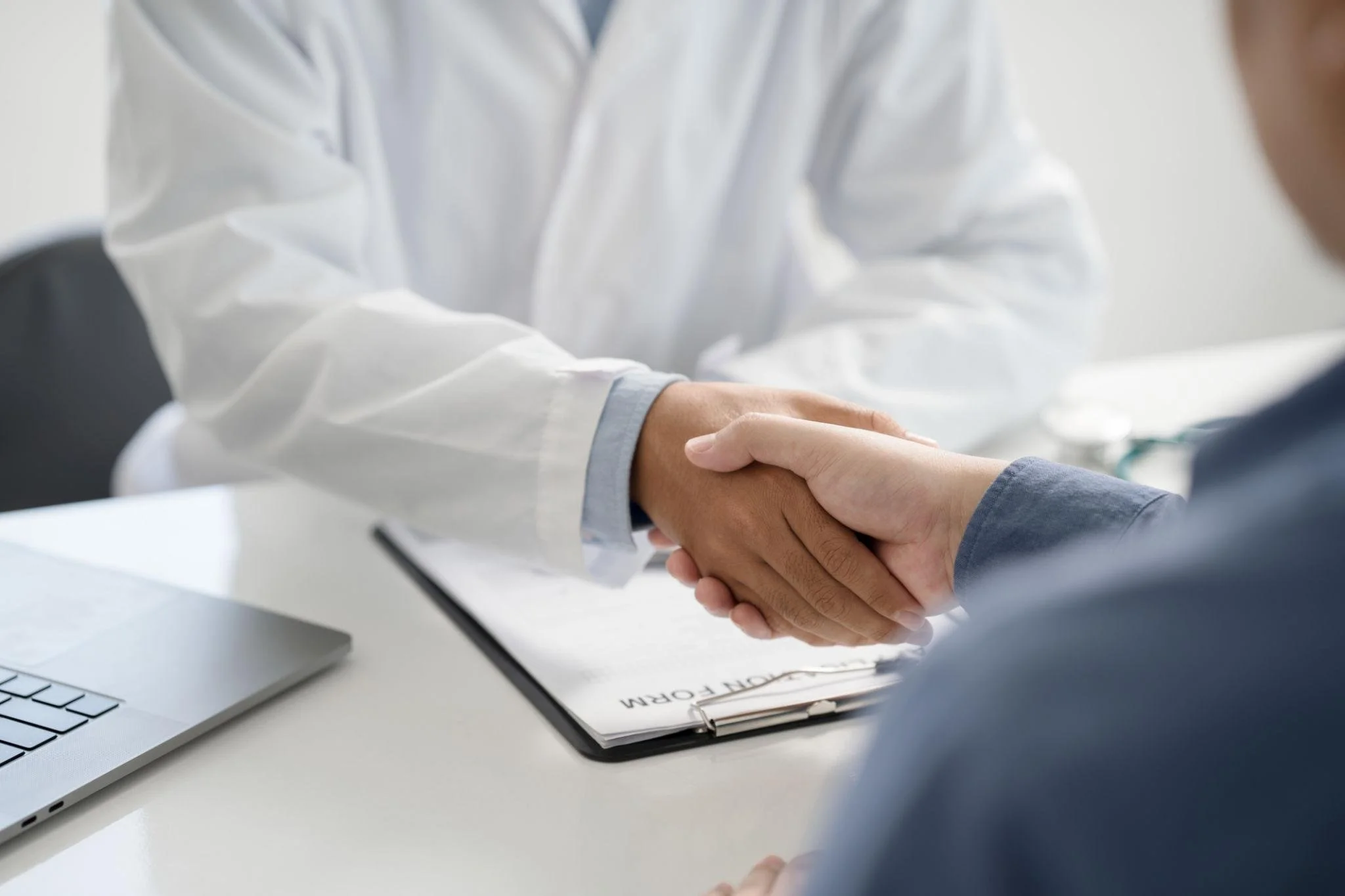 Pessoa de terno e médico apertando as mãos em assinatura de contrato no escritório.