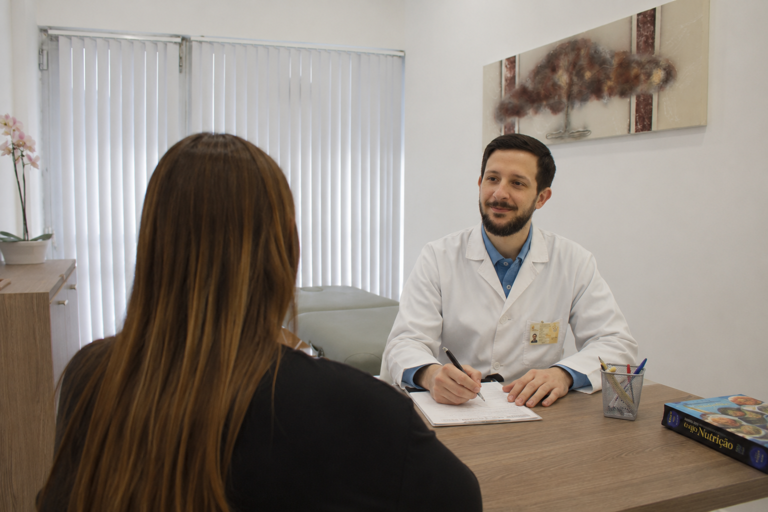 Médico conversando com uma paciente em consultório, com livros e canetas na mesa
