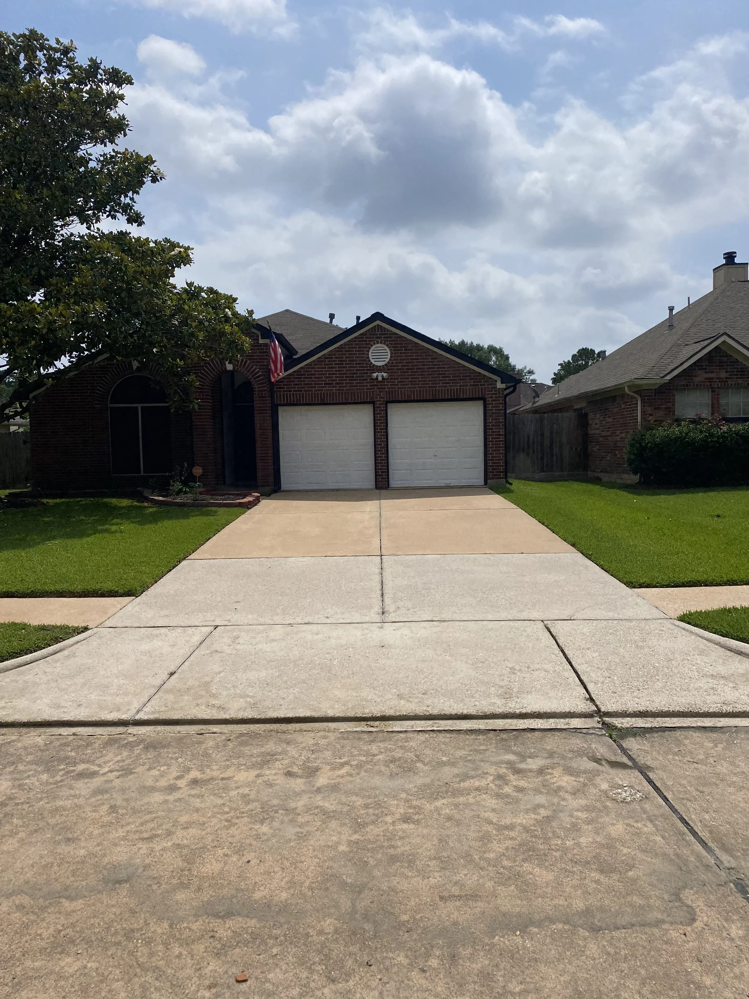 Freshly cleaned driveway in front of a red brick home in Houston, TX, showing bright, uniform concrete after professional pressure washing by Wyatt Washes