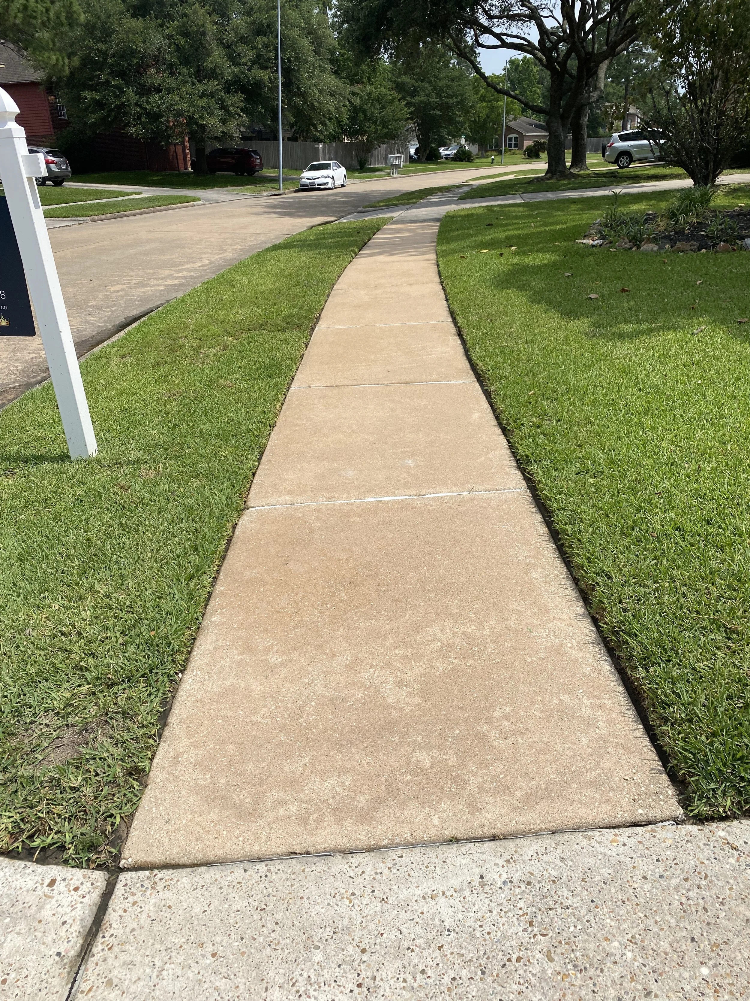Clean, bright sidewalk in front of a Houston, TX home after professional pressure washing by Wyatt Washes, showing refreshed concrete and neat lawn edging.